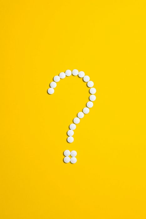 Question mark made of white pills on a yellow background.