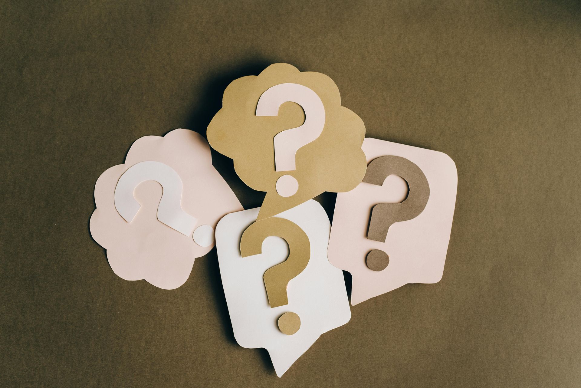 Cut-out question marks in various colors and speech bubbles on a green-brown background.