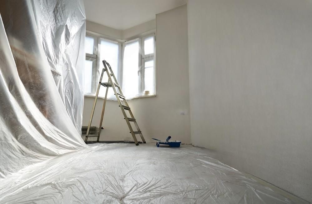 An empty room with a ladder and a sheet of plastic on the floor.