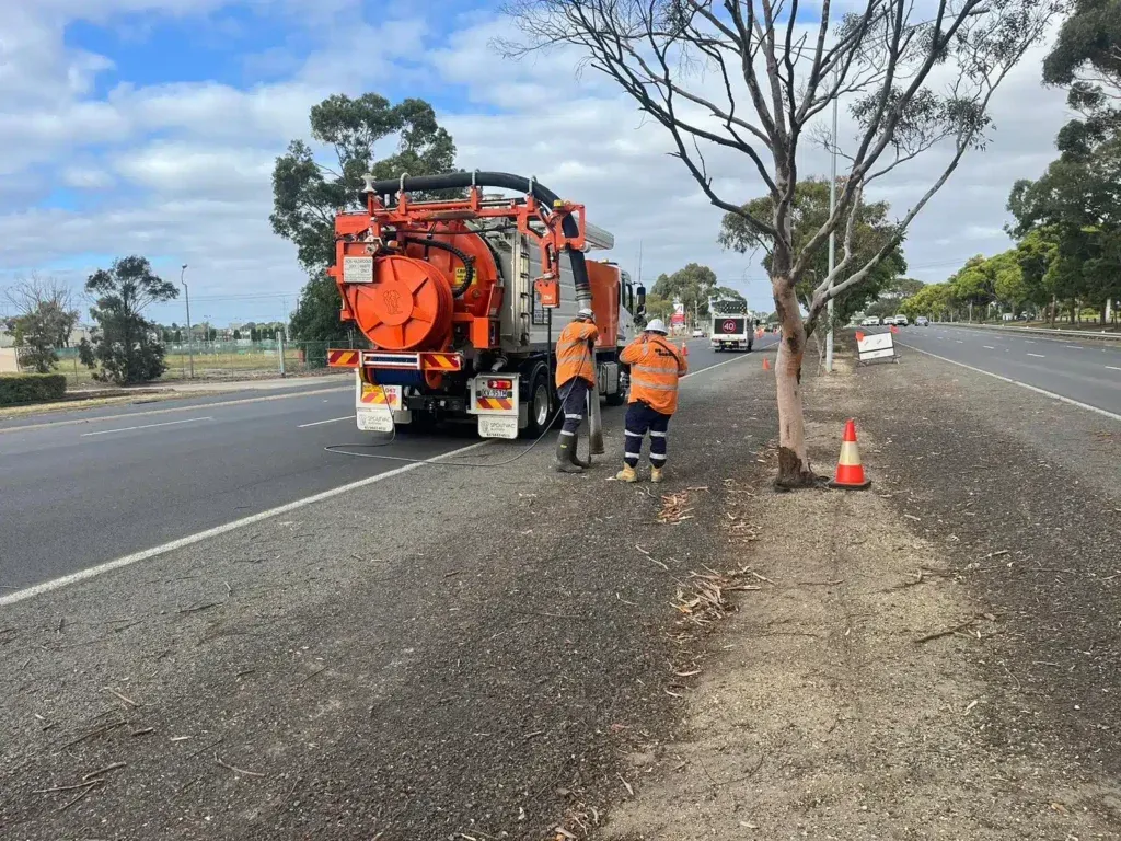 A vacuum truck is parked on the side of the road next to a tree.