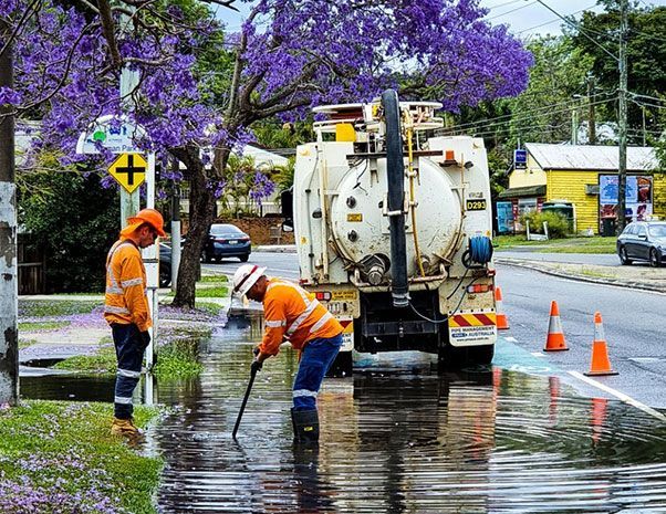 Two men are cleaning a puddle on the side of the road.