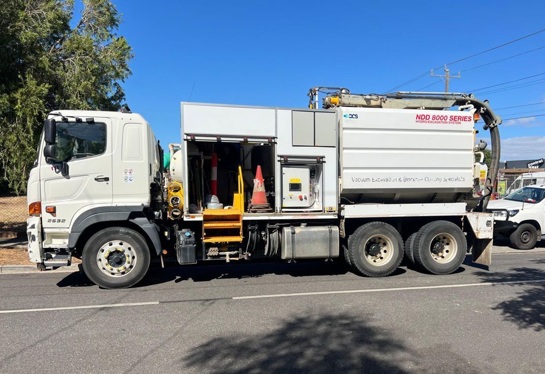 A vacuum truck is parked on the side of the road next to a tree.