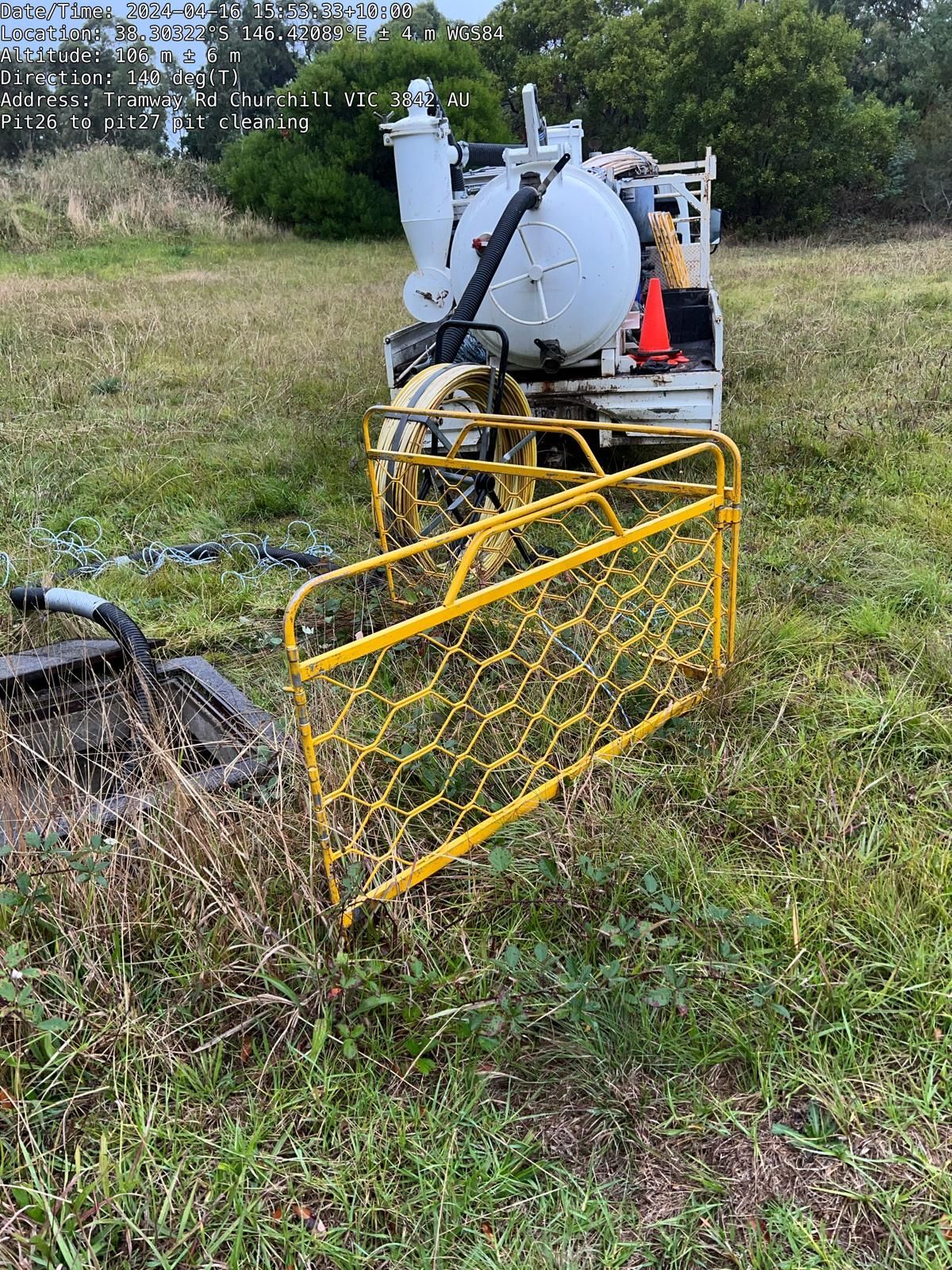 A vacuum truck is parked in a grassy field next to a yellow fence.