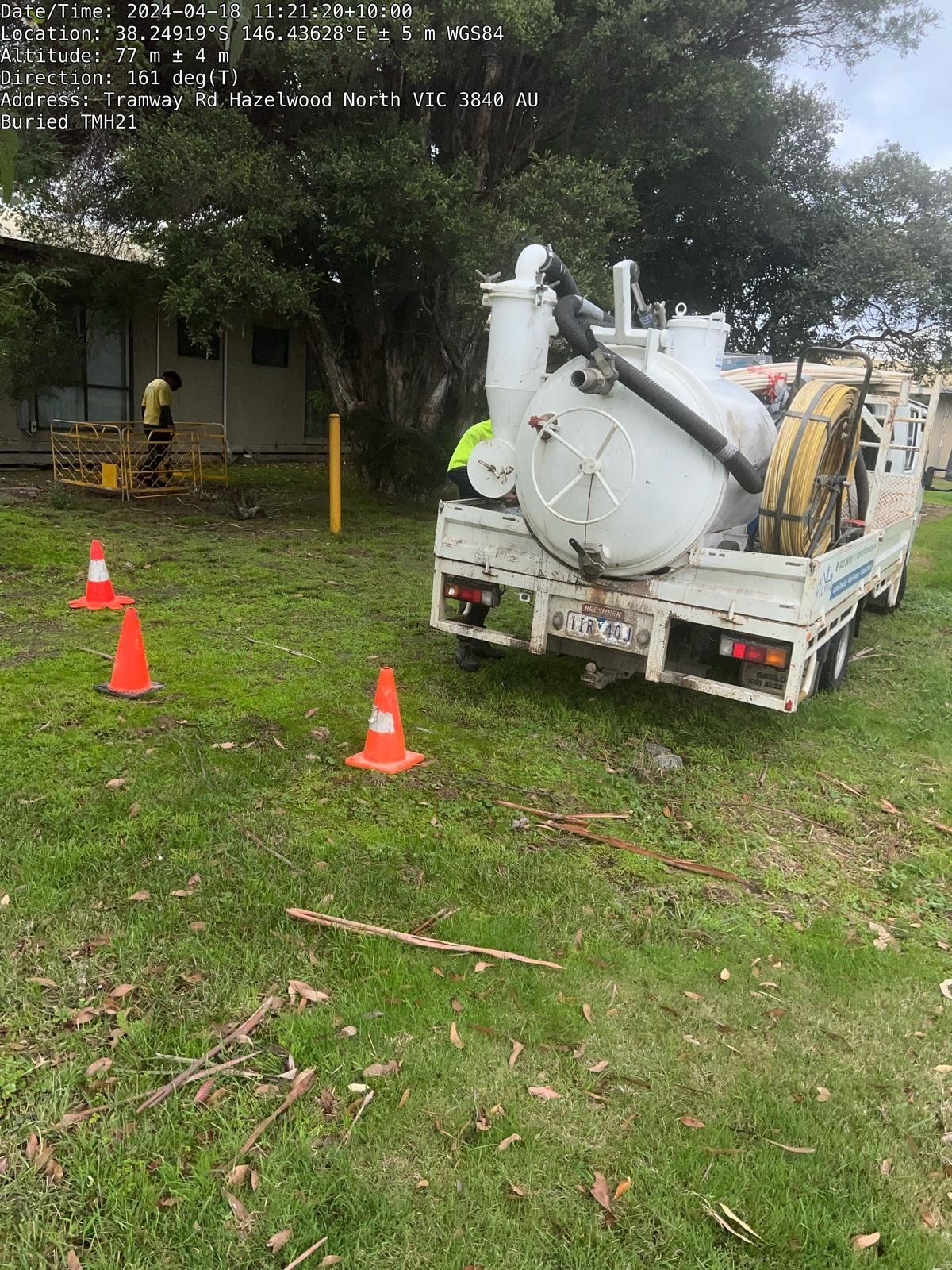 A vacuum truck is parked in a grassy field next to traffic cones.