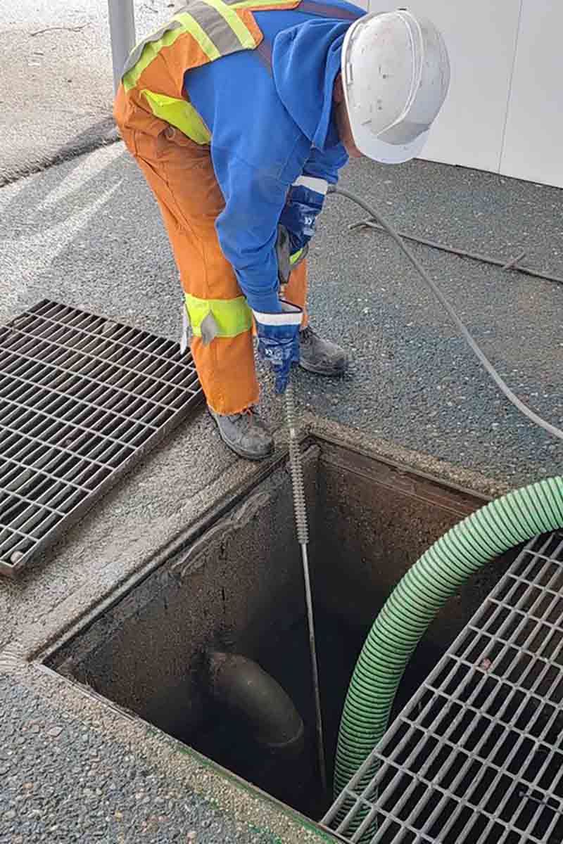 A man is working on a manhole cover with a hose.