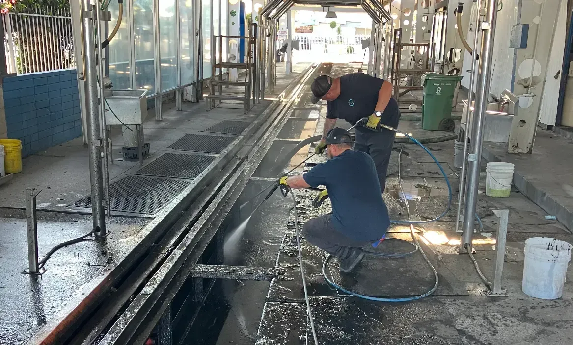 Two men are cleaning a train track with a hose.