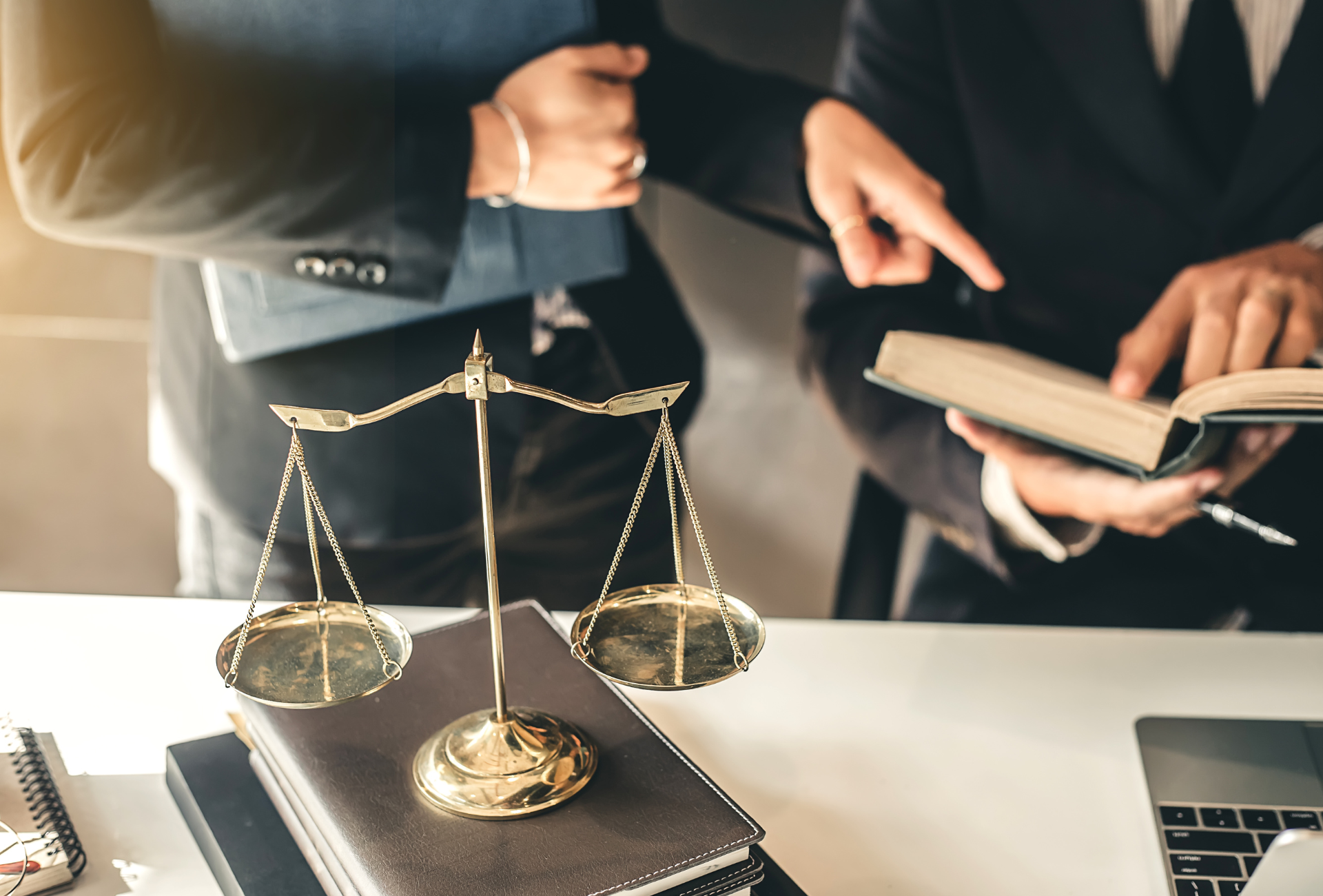 two lawyers are looking at a book and a scale of justice on a desk .