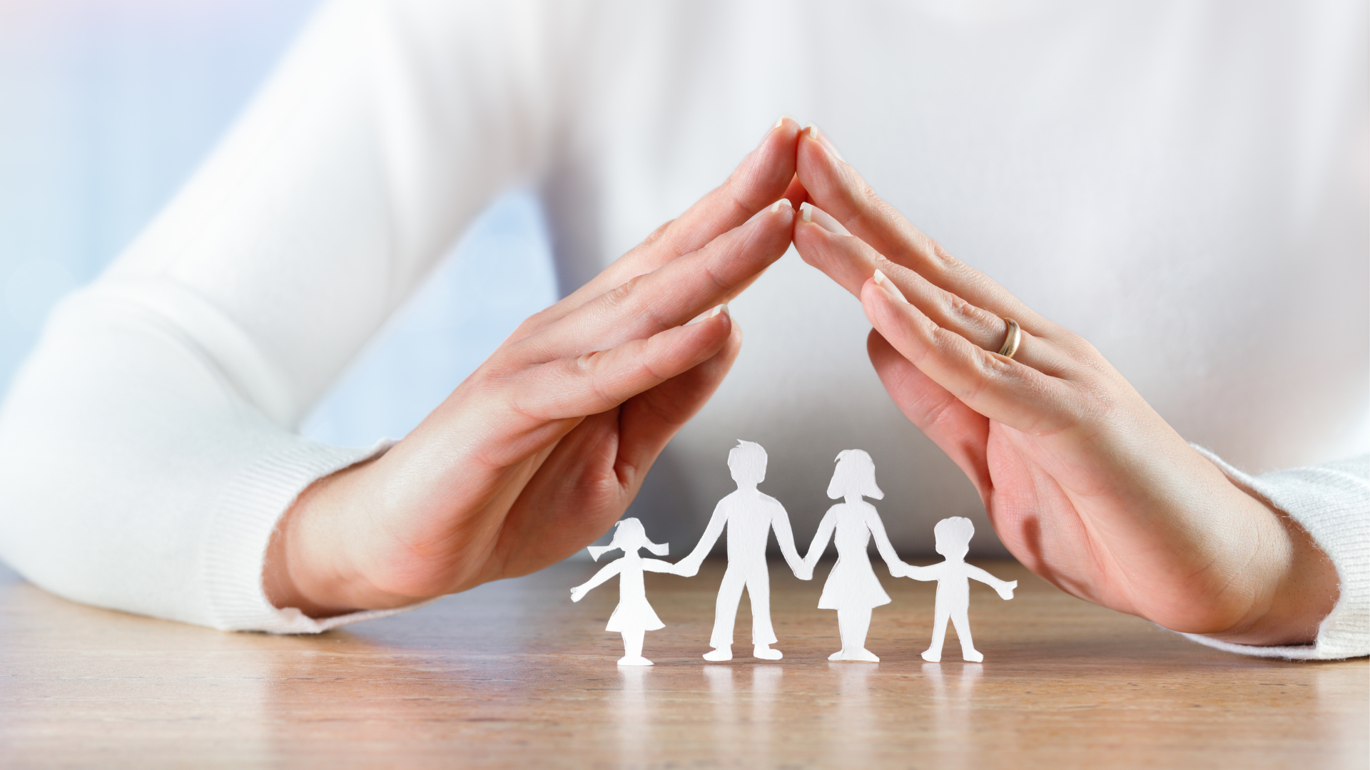 a person is covering a paper cut out of a family with their hands .