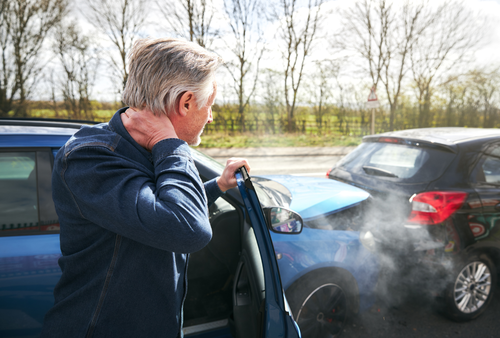 a man is standing in front of a car that has smoke coming out of it .