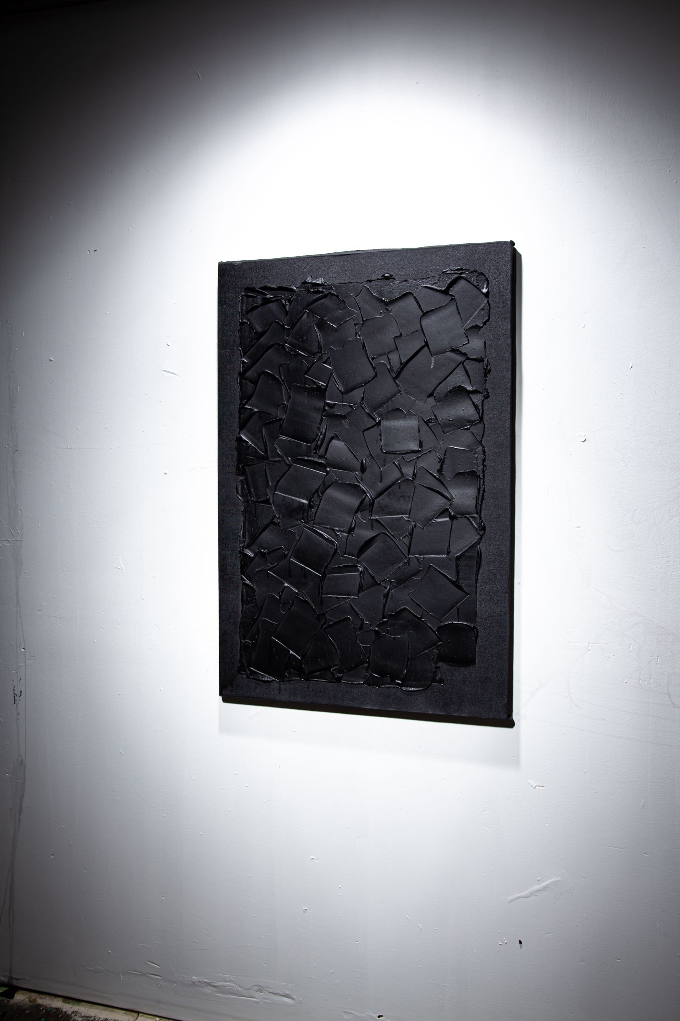 Black textured artwork on a white wall, lit by a spotlight; art by Matt Remsbecher. 
