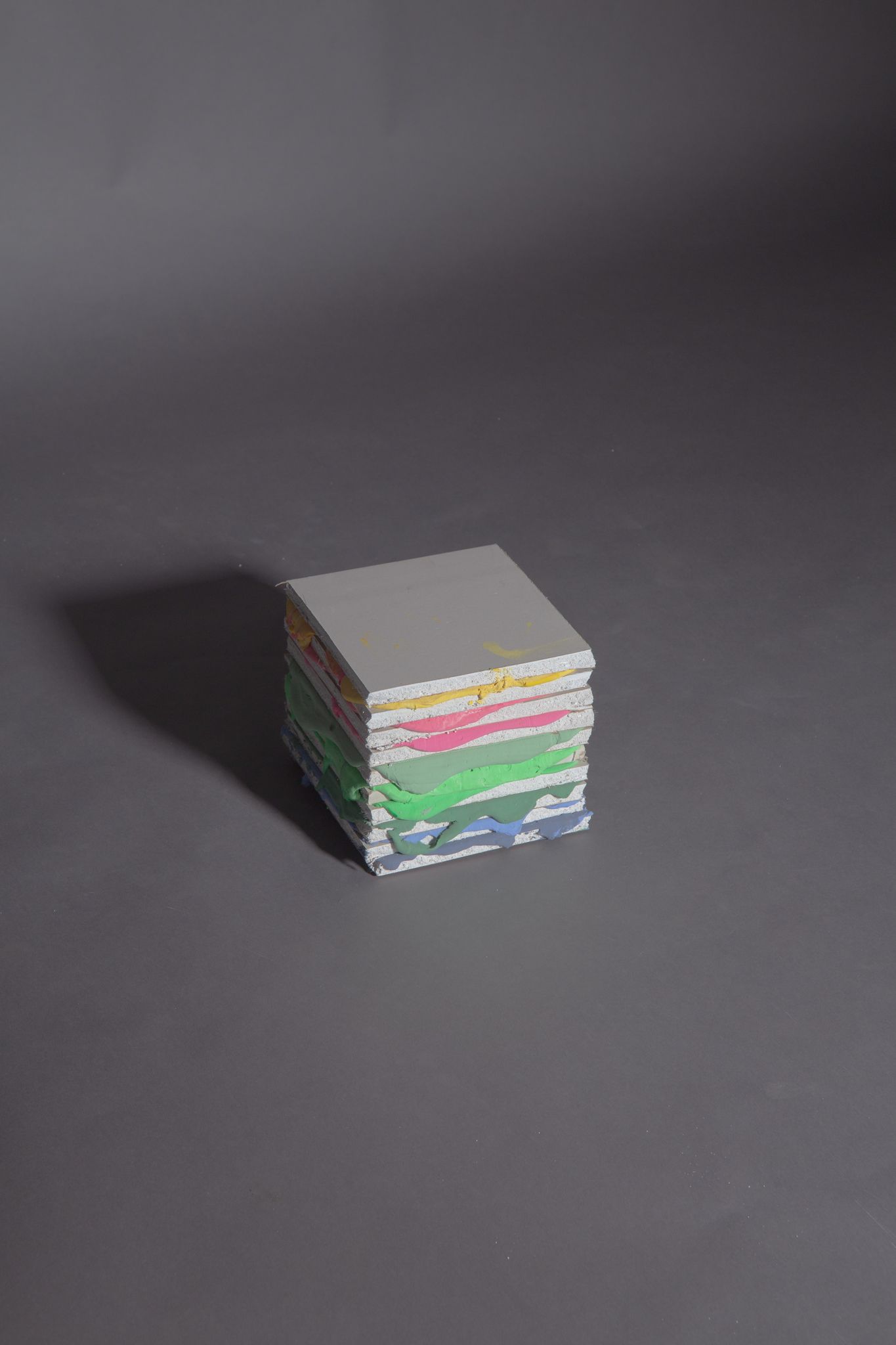A stack of colorful, rectangular paper on a gray surface, casting a shadow; art by Matt Remsbecher. 