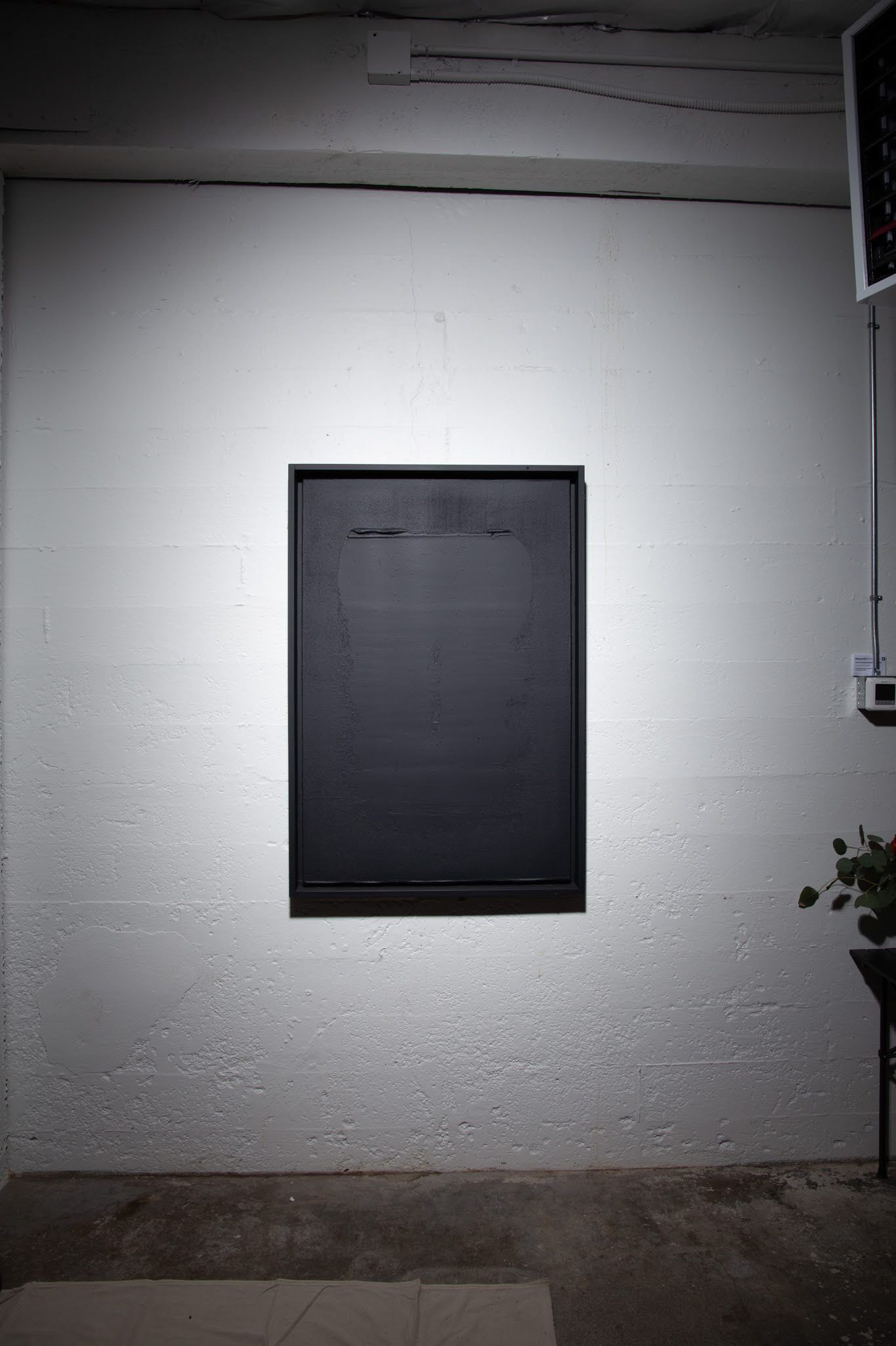 Black rectangle on a white wall, lit by a spotlight.  Setting appears to be a room interior; art by Matt Remsbecher. 