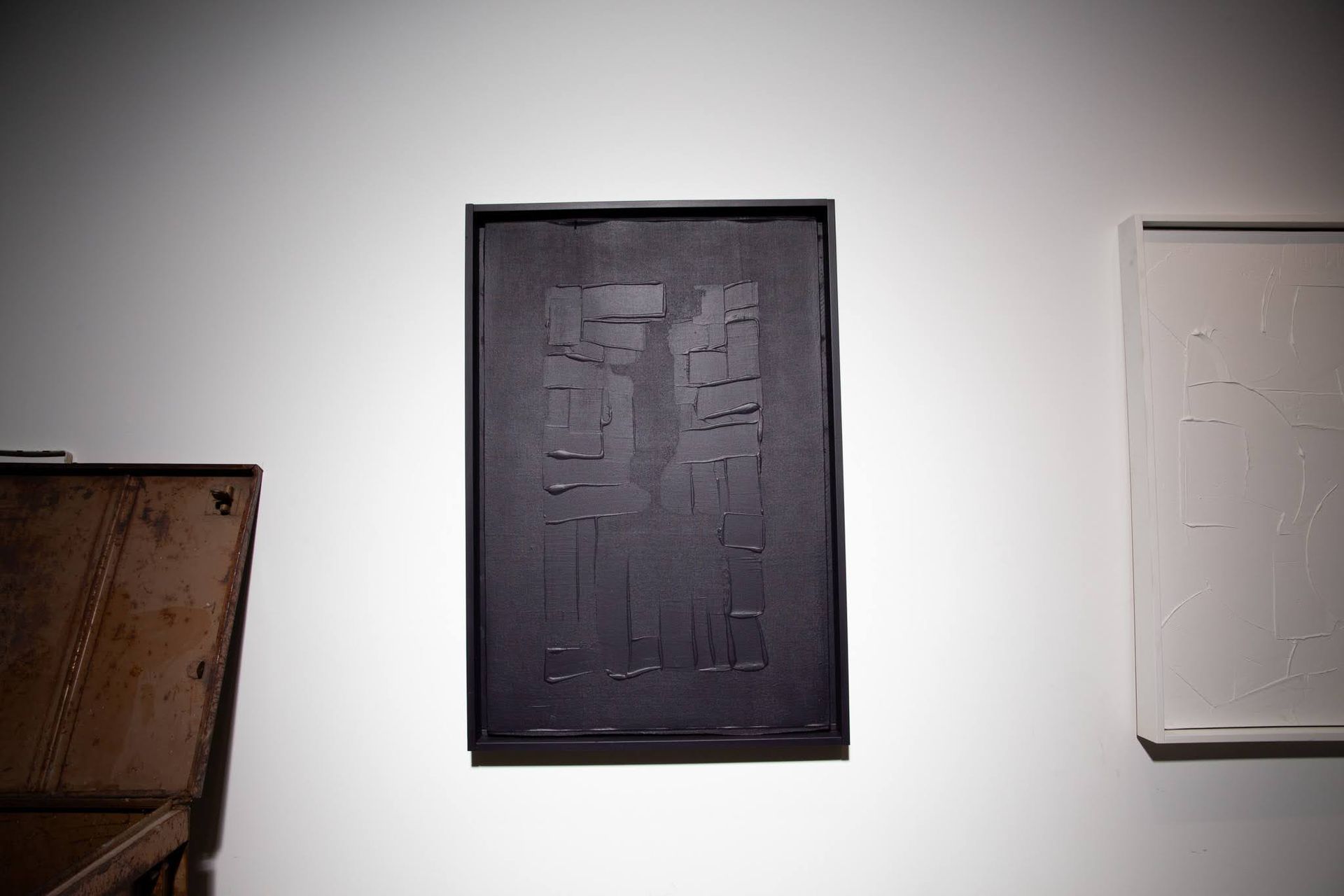 Dark artwork on white wall, rectangular, textured black paint with white painting to the right; art by Matt Remsbecher. 