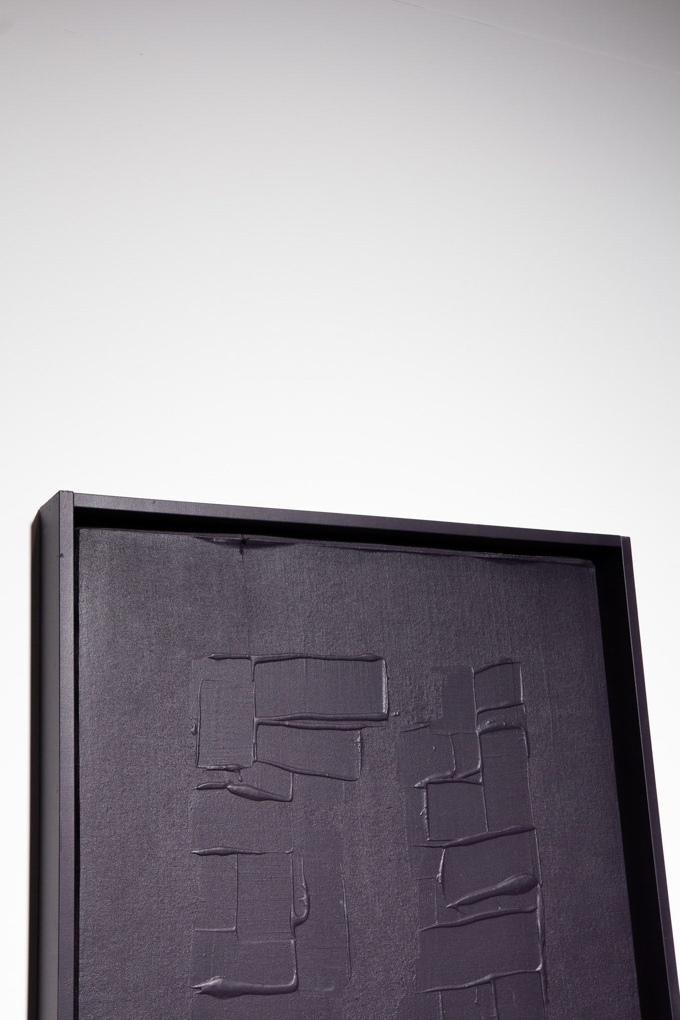Black, textured art piece with a recessed design, framed, against a white background; art by Matt Remsbecher. 
