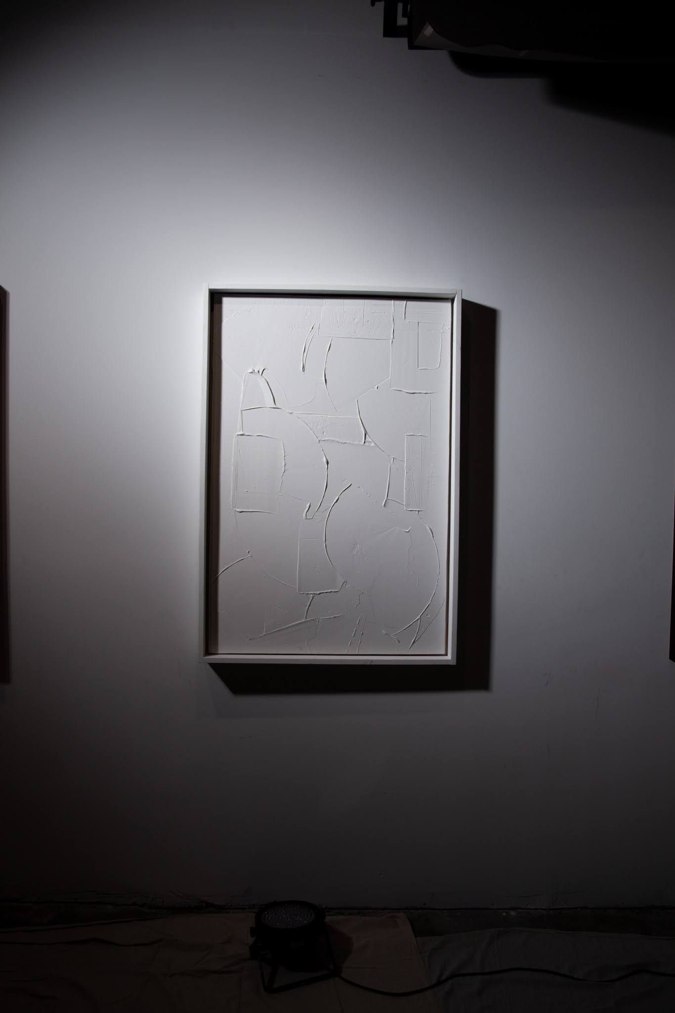 White framed artwork on a white wall, dimly lit with scattered dark shapes; gallery setting; art by Matt Remsbecher. 