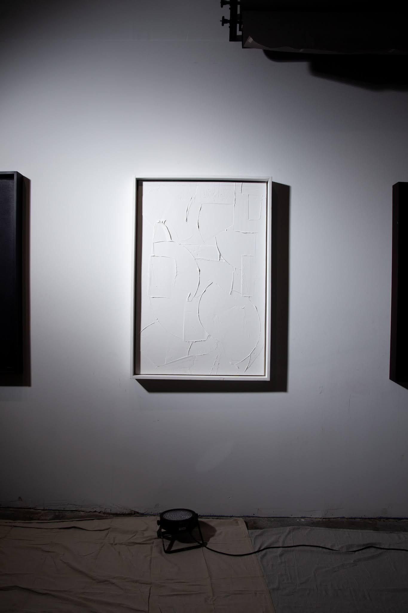 White abstract art in a frame on a white wall. Dark shadows and another black frame visible; art by Matt Remsbecher. 