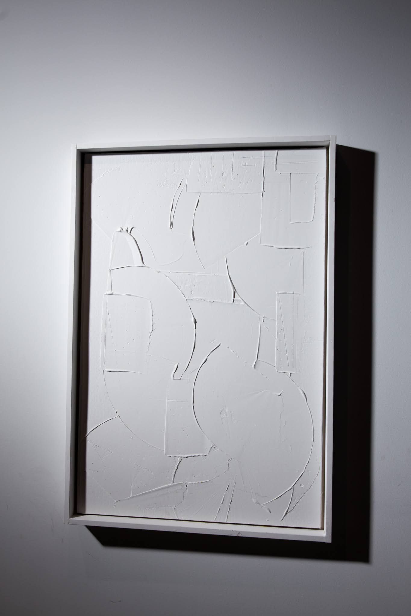 White framed relief art with a geometric design hanging on a white wall; art by Matt Remsbecher. 