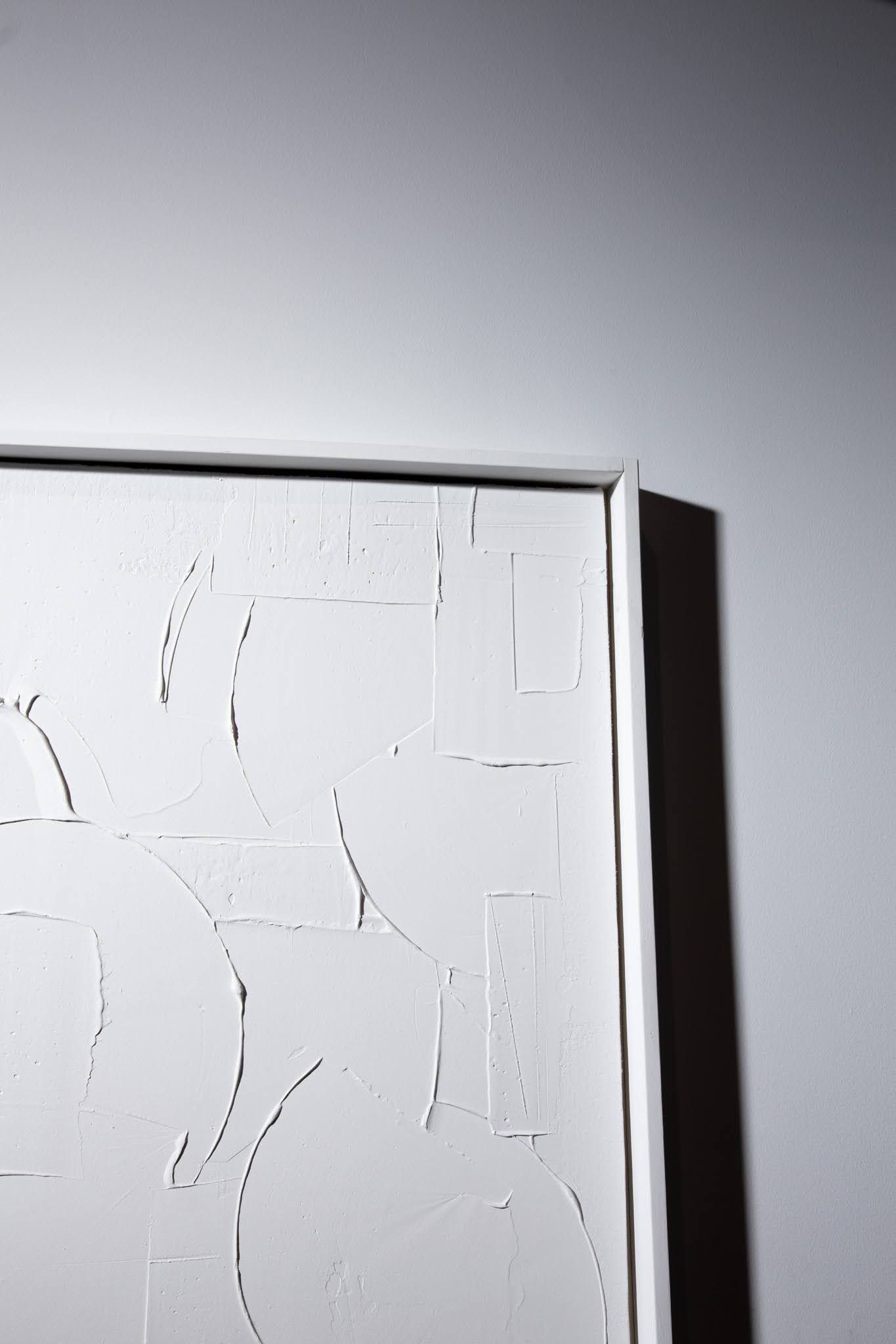 Close-up of a white textured artwork in a white frame, displayed against a light gray wall; art by Matt Remsbecher. 