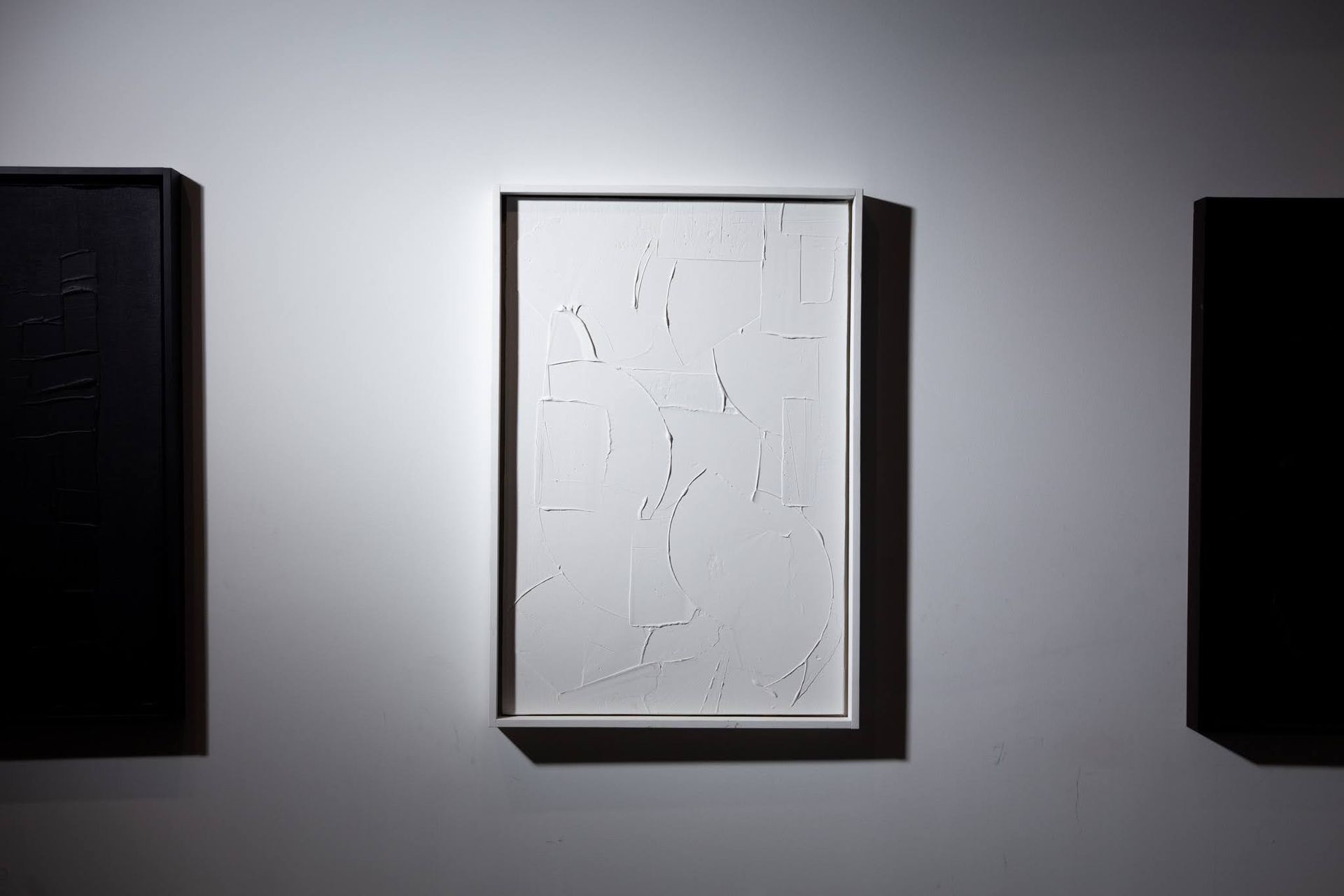 Three framed abstract paintings on a white wall; central artwork is white with dark lines; art by Matt Remsbecher. 