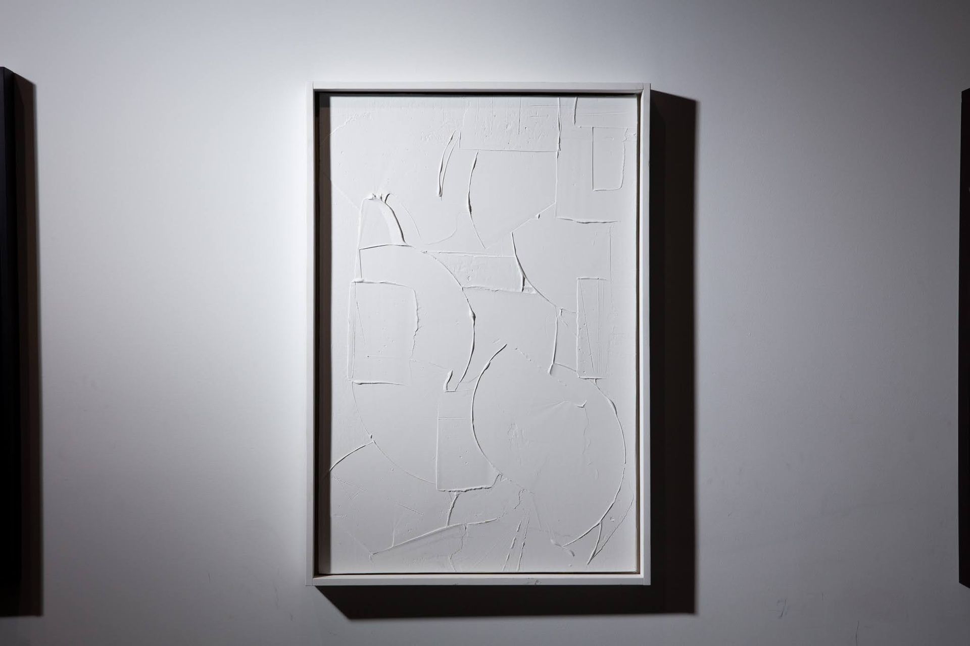 White abstract artwork in a white frame, against a gray wall; art by Matt Remsbecher. 