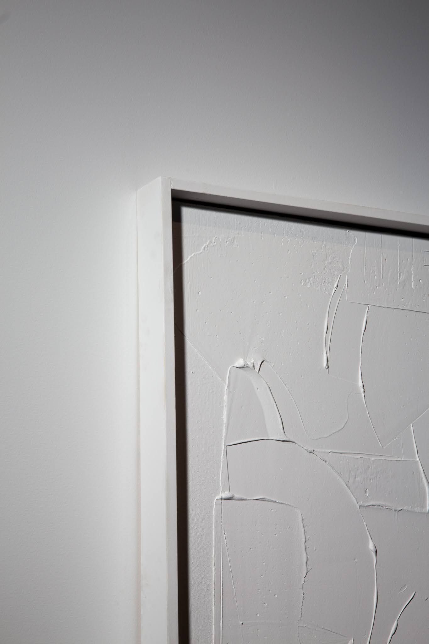 White textured artwork in a black frame, mounted on a white wall; art by Matt Remsbecher. 
