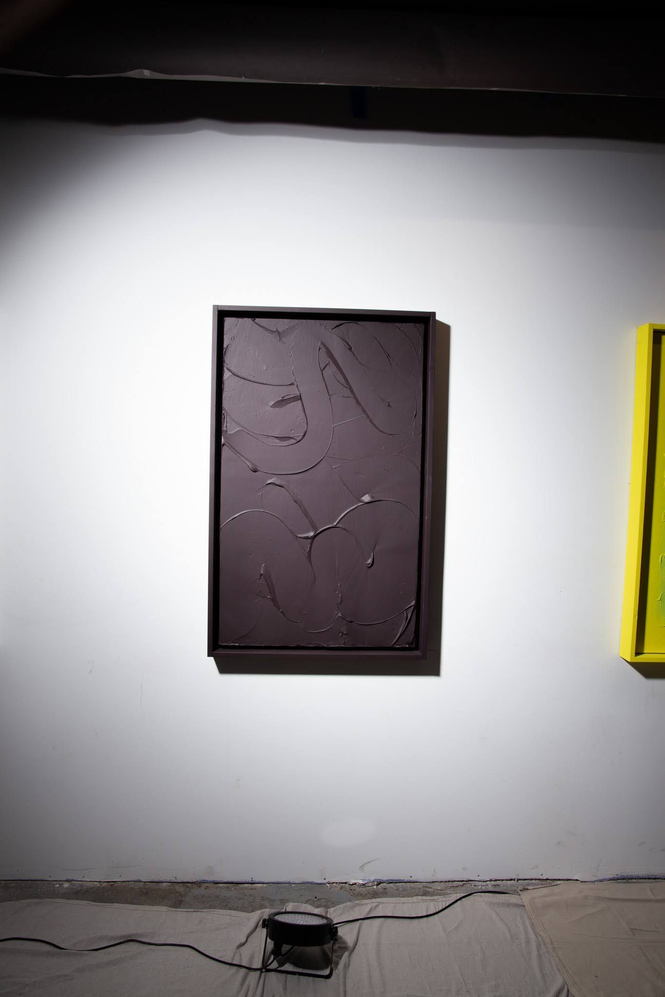 Dark framed abstract art on white wall, illuminated by spotlight; art by Matt Remsbecher. 