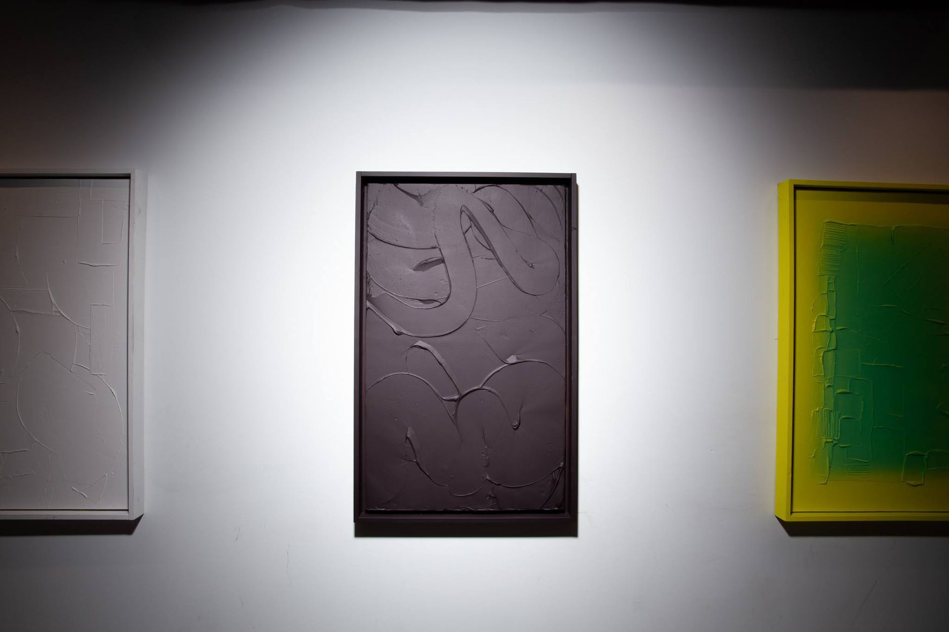 Three framed abstract paintings on a white wall; central painting is dark; art by Matt Remsbecher. 