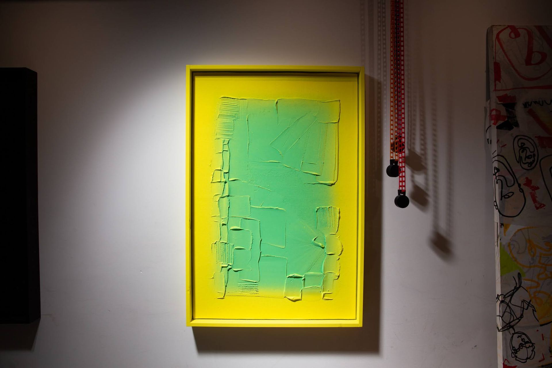 Green abstract art in a yellow frame on a white wall, with a red string hanging nearby; art by Matt Remsbecher.