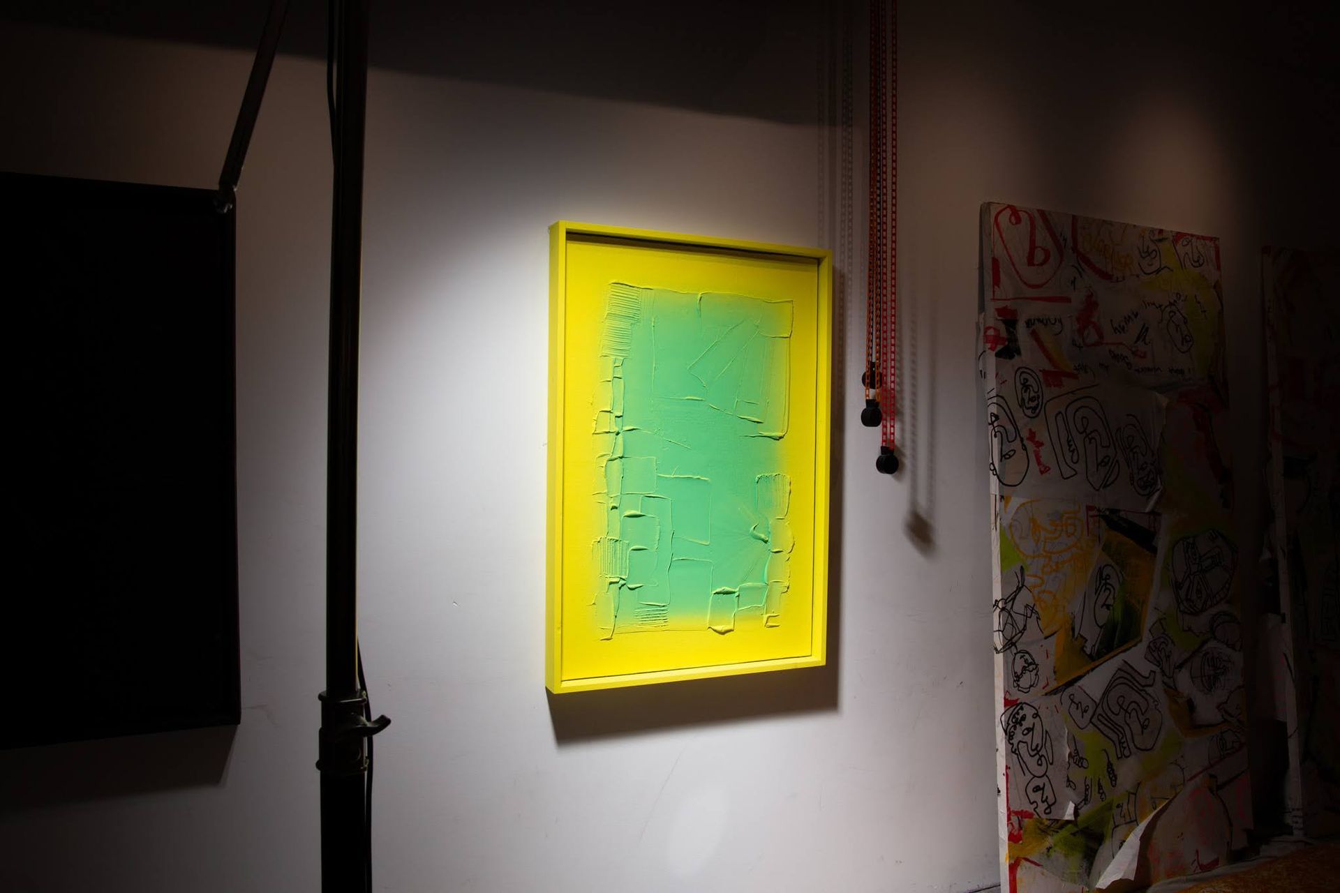 Yellow-framed artwork with green textured center hangs on a white wall; art by Matt Remsbecher. 