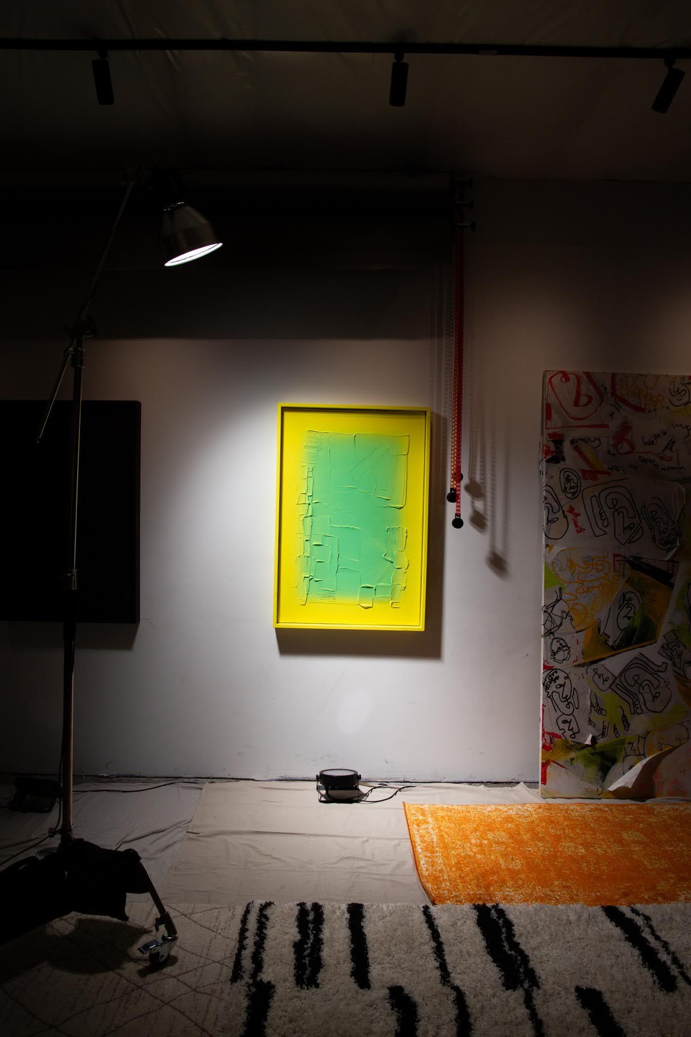 Yellow-framed artwork with green center hangs on a white wall in a room; art by Matt Remsbecher. 