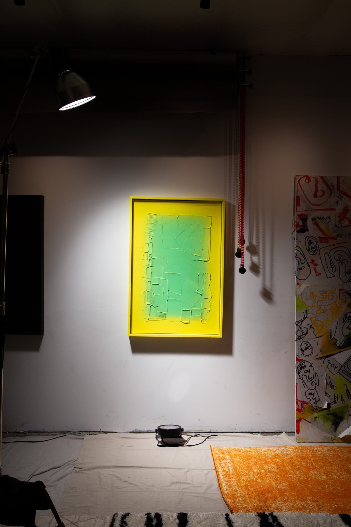 Green and yellow abstract painting on a white wall, lit by a spotlight, in an art gallery; art by Matt Remsbecher. 