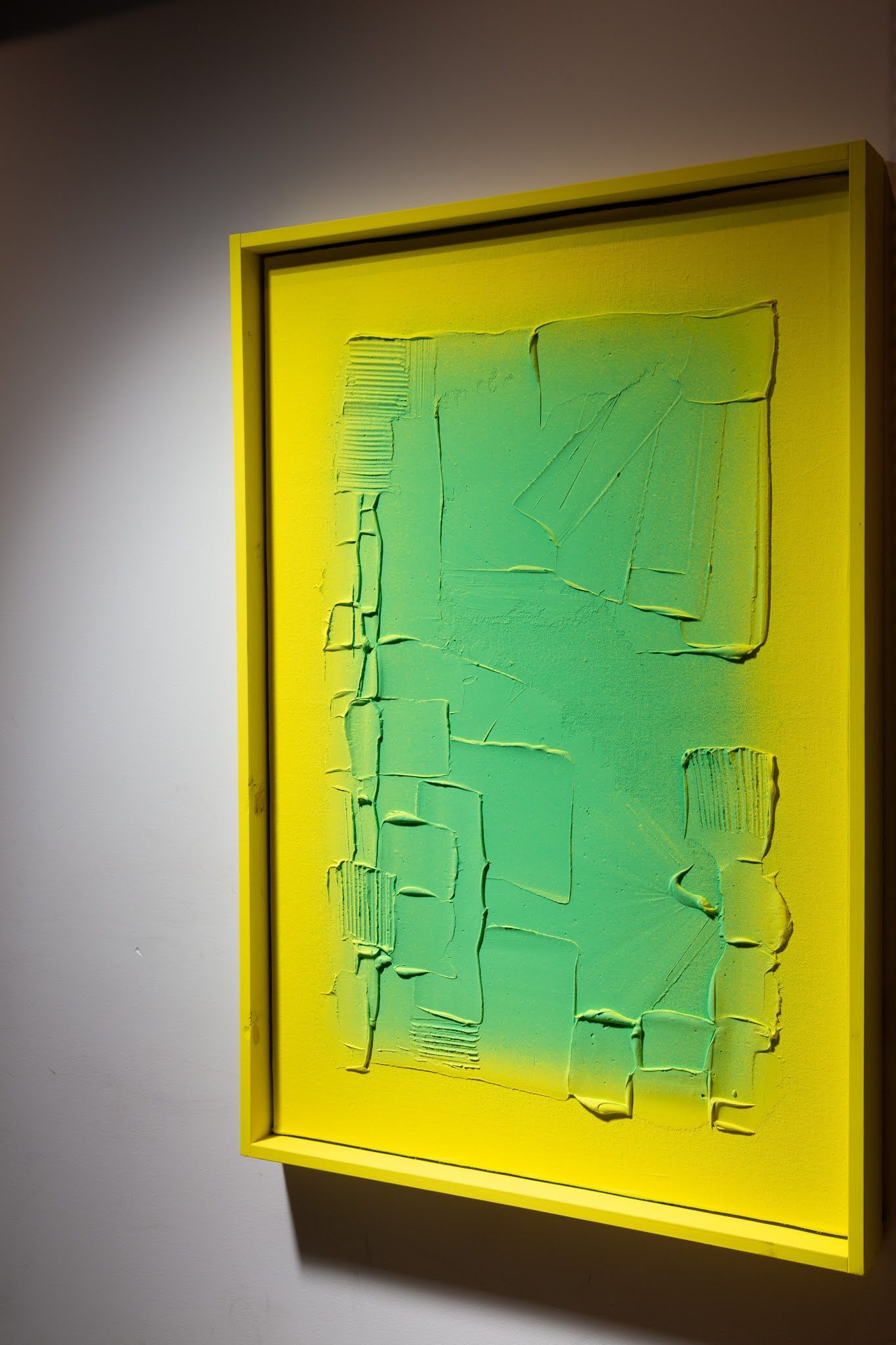 Yellow framed artwork: green textured rectangle on yellow background. Wall-mounted, lit from left; art by Matt Remsbecher. 