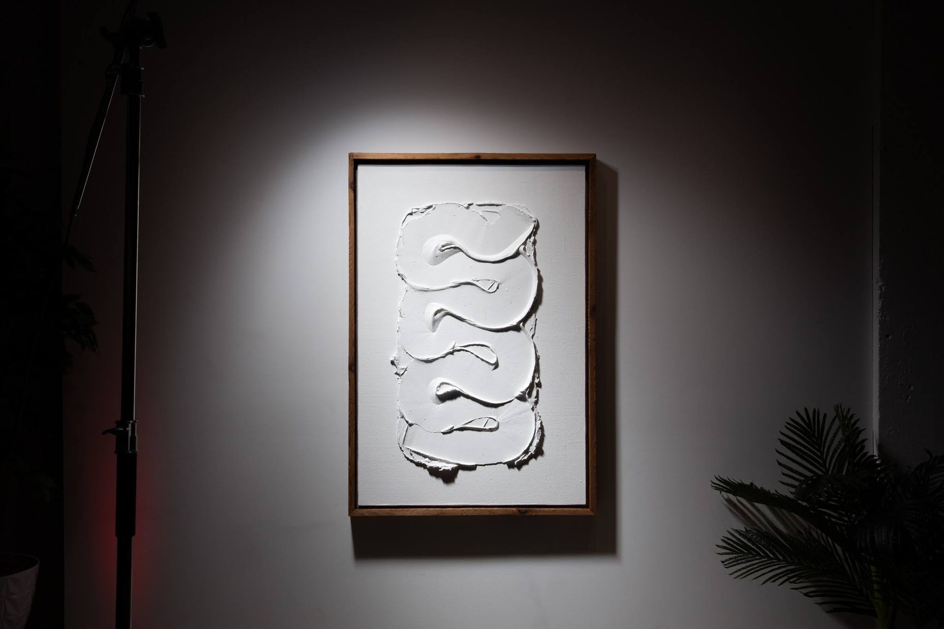 White textured art piece in a wooden frame lit by a spotlight; art by Matt Remsbecher. 