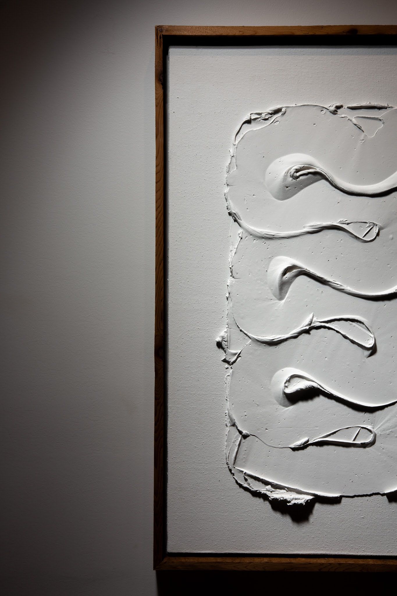 Textured white artwork in wooden frame on a gray wall, creating abstract vertical shapes; art by Matt Remsbecher. 