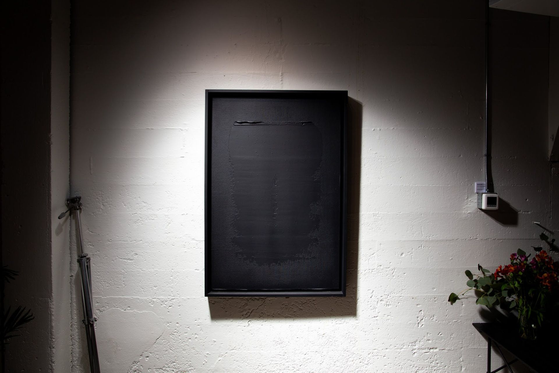Black framed artwork on a textured wall, spotlit. Sparse lines etched on the black surface; art by Matt Remsbecher. 