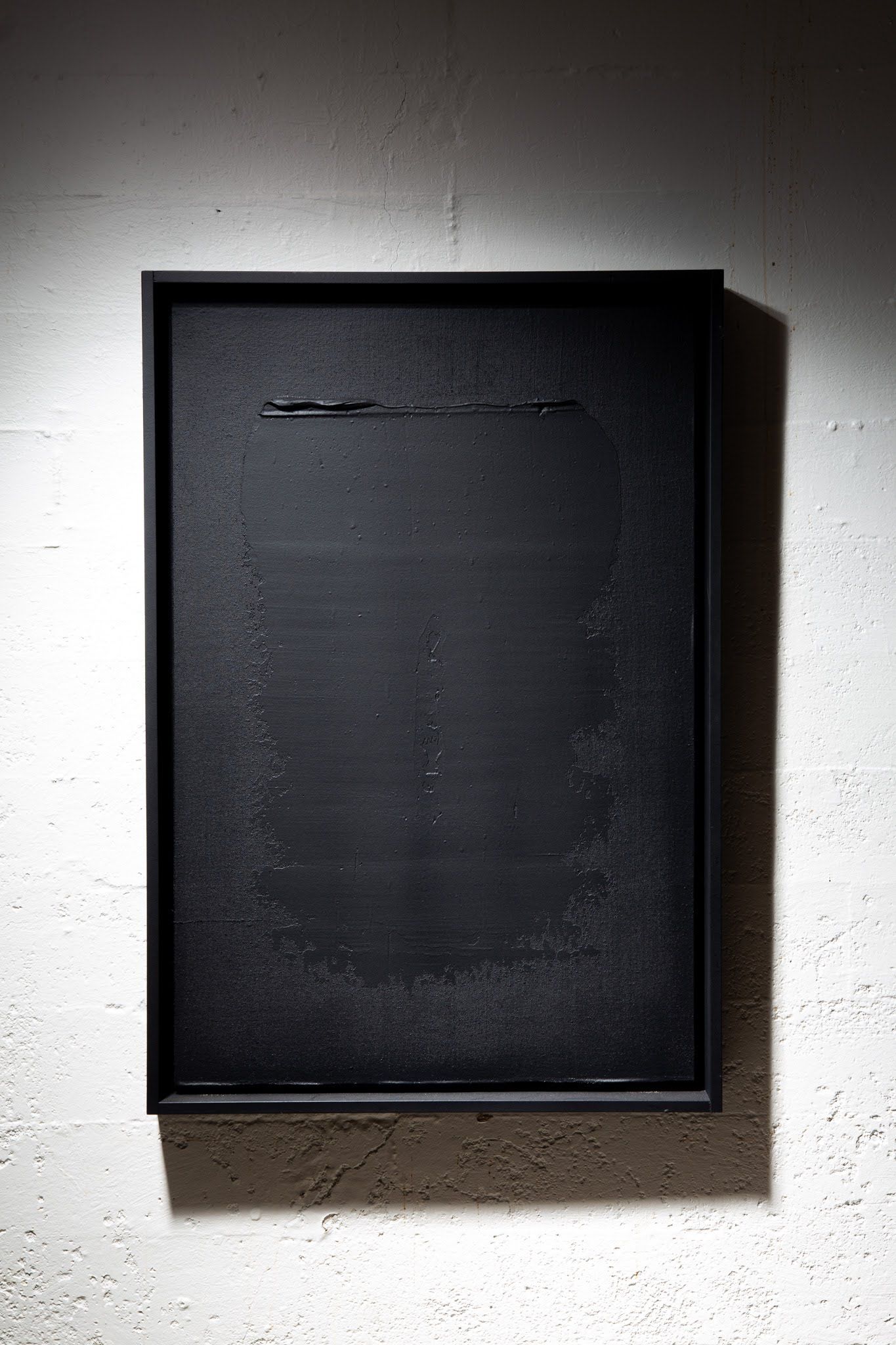 Black abstract painting in a black frame, mounted on a white, textured wall; art by Matt Remsbecher. 