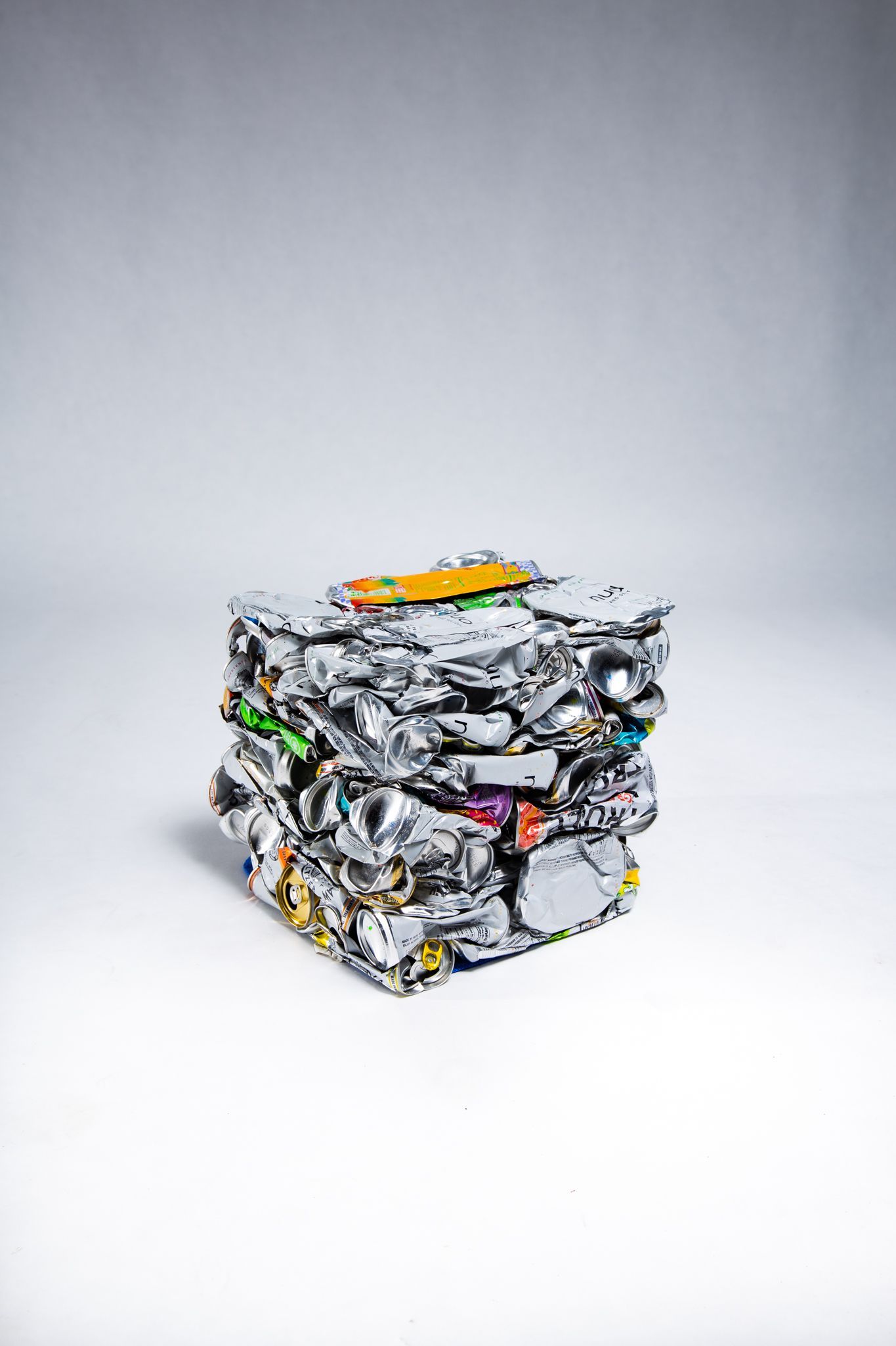 Compressed cube of aluminum foil and packaging on a white surface, showing various colors; art by Matt Remsbecher. 