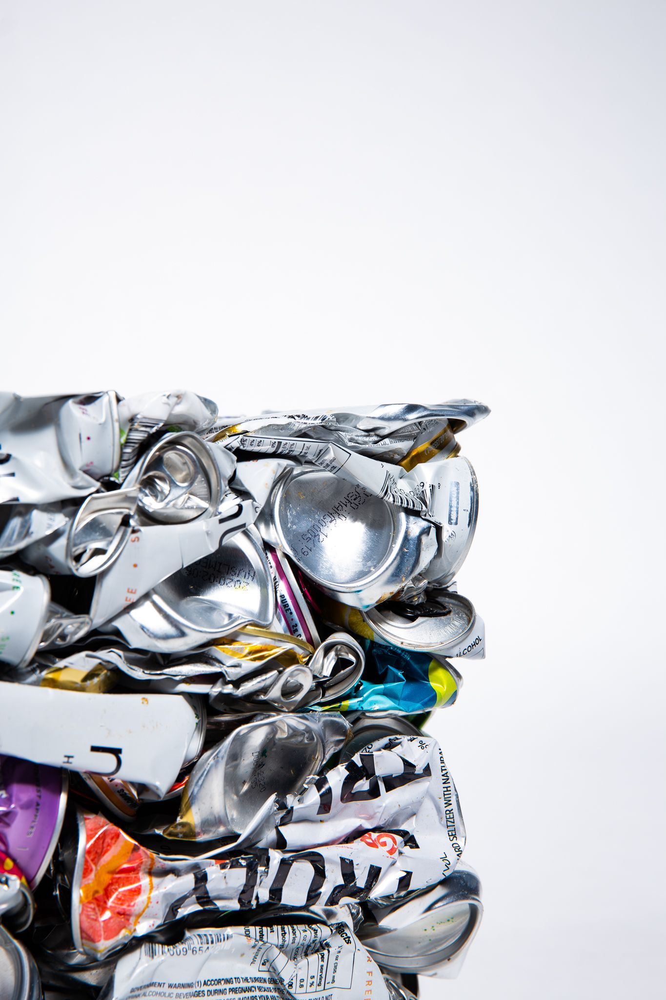 Crushed aluminum cans compressed into a cube, against a white backdrop; art by Matt Remsbecher. 