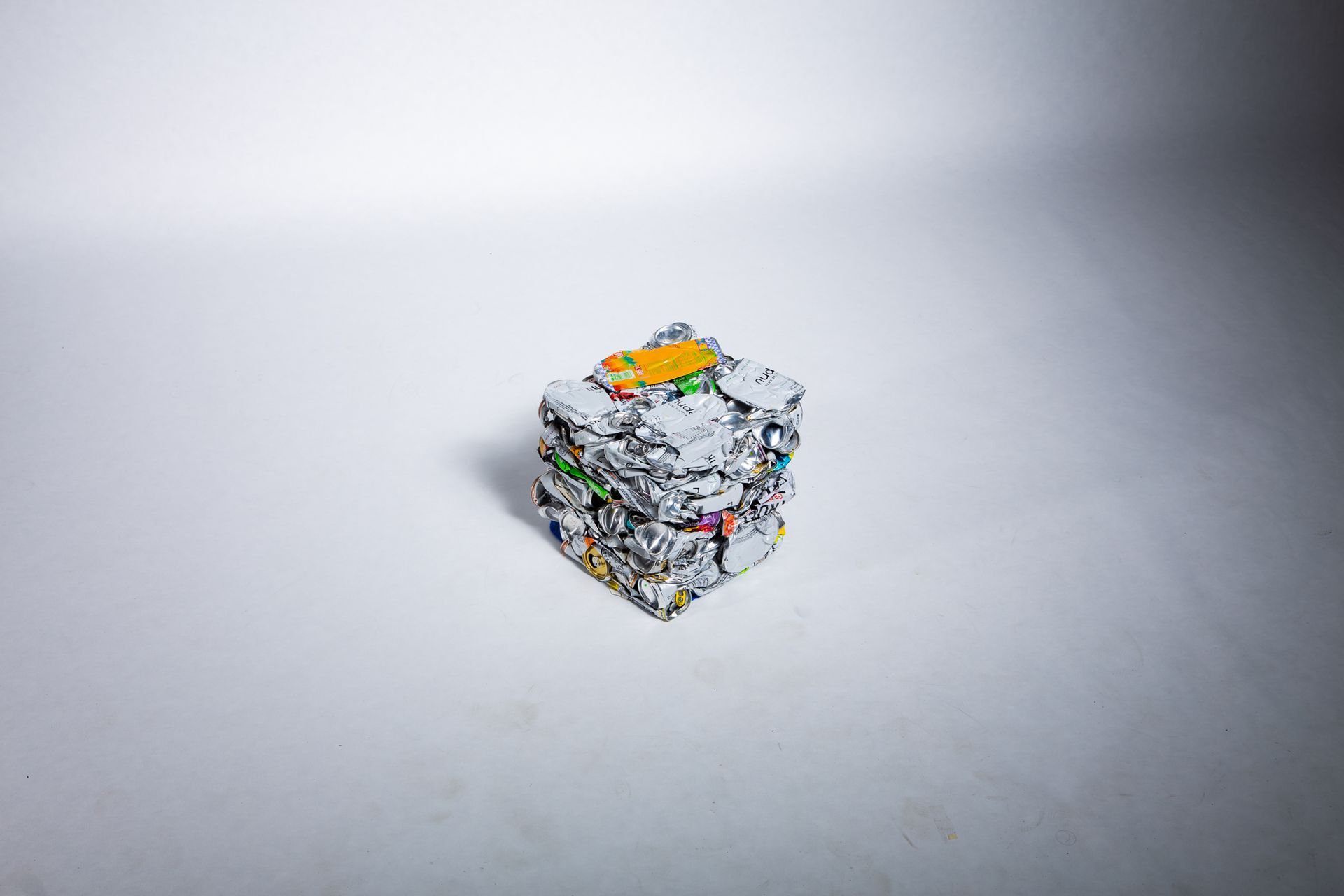 Pile of crumpled, silver and colorful materials in a cube shape, with a yellow item on top; art by Matt Remsbecher. 