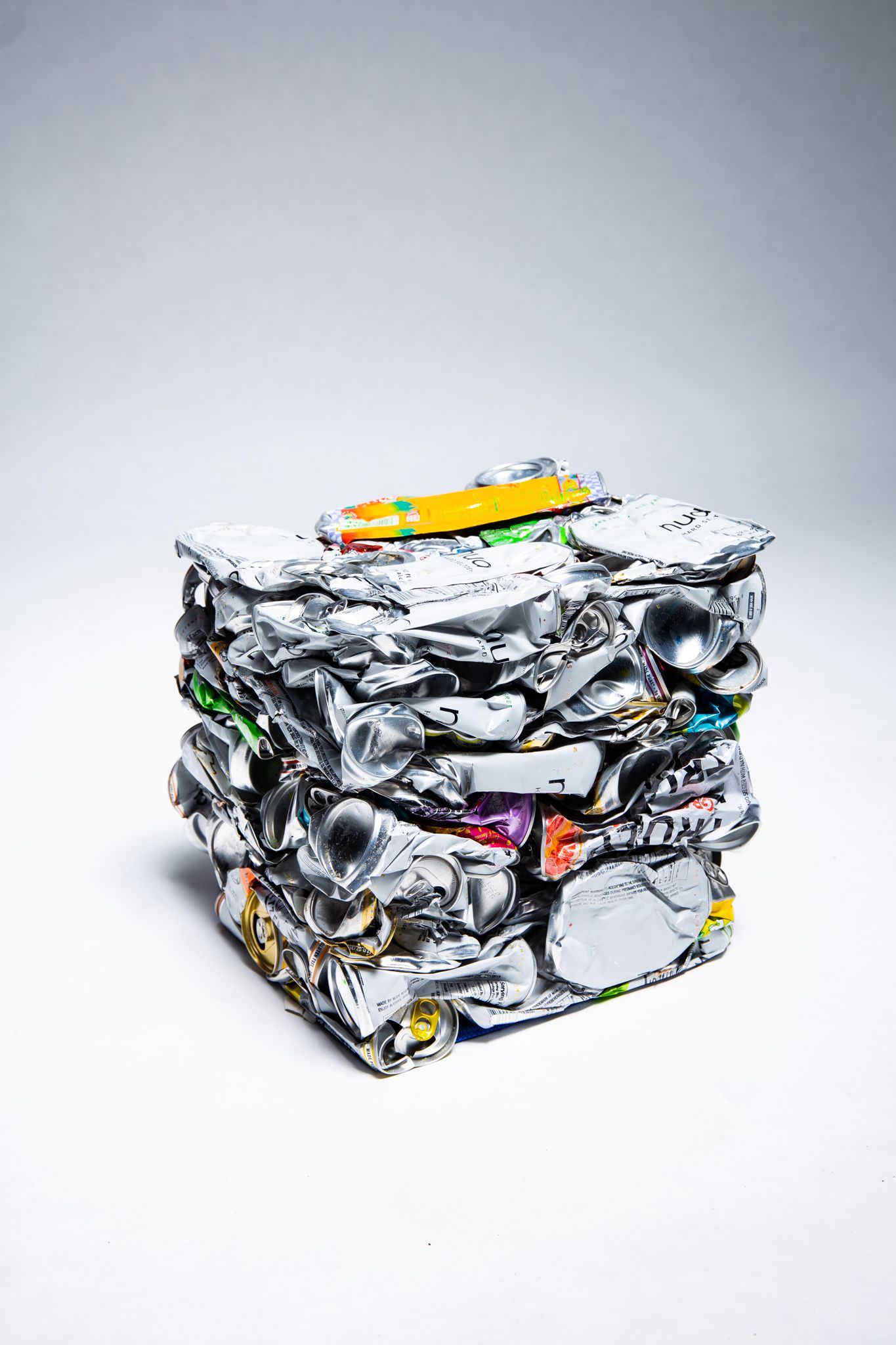 A cube of crushed aluminum cans with a pencil on top; art by Matt Remsbecher. 