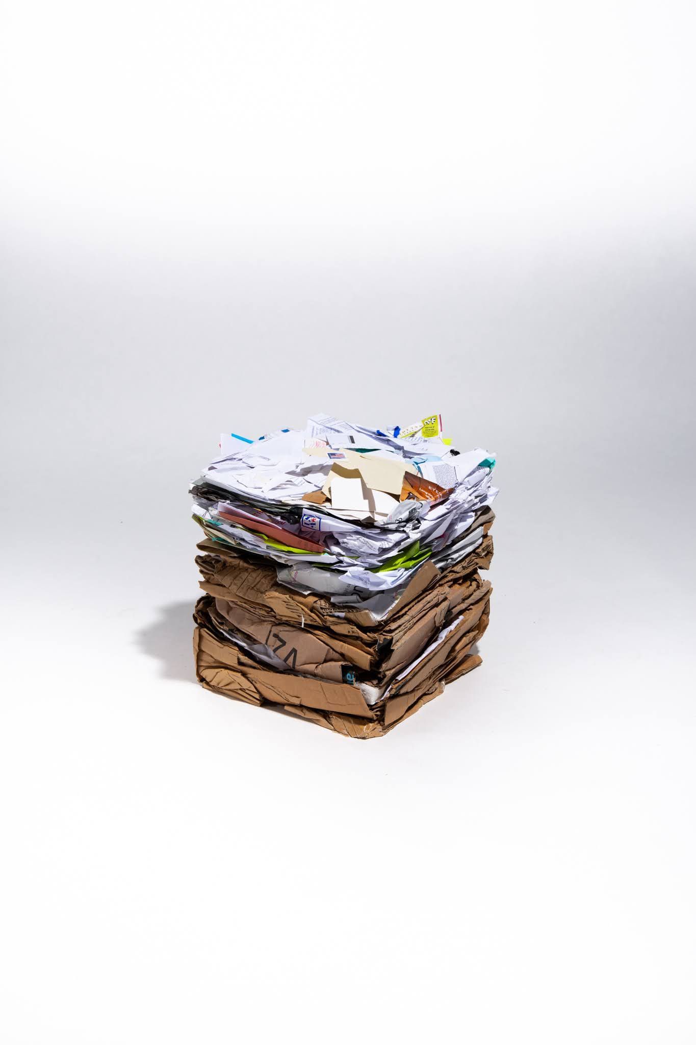 Stack of mixed paper and cardboard on a white background, lit by a single light source; art by Matt Remsbecher. 