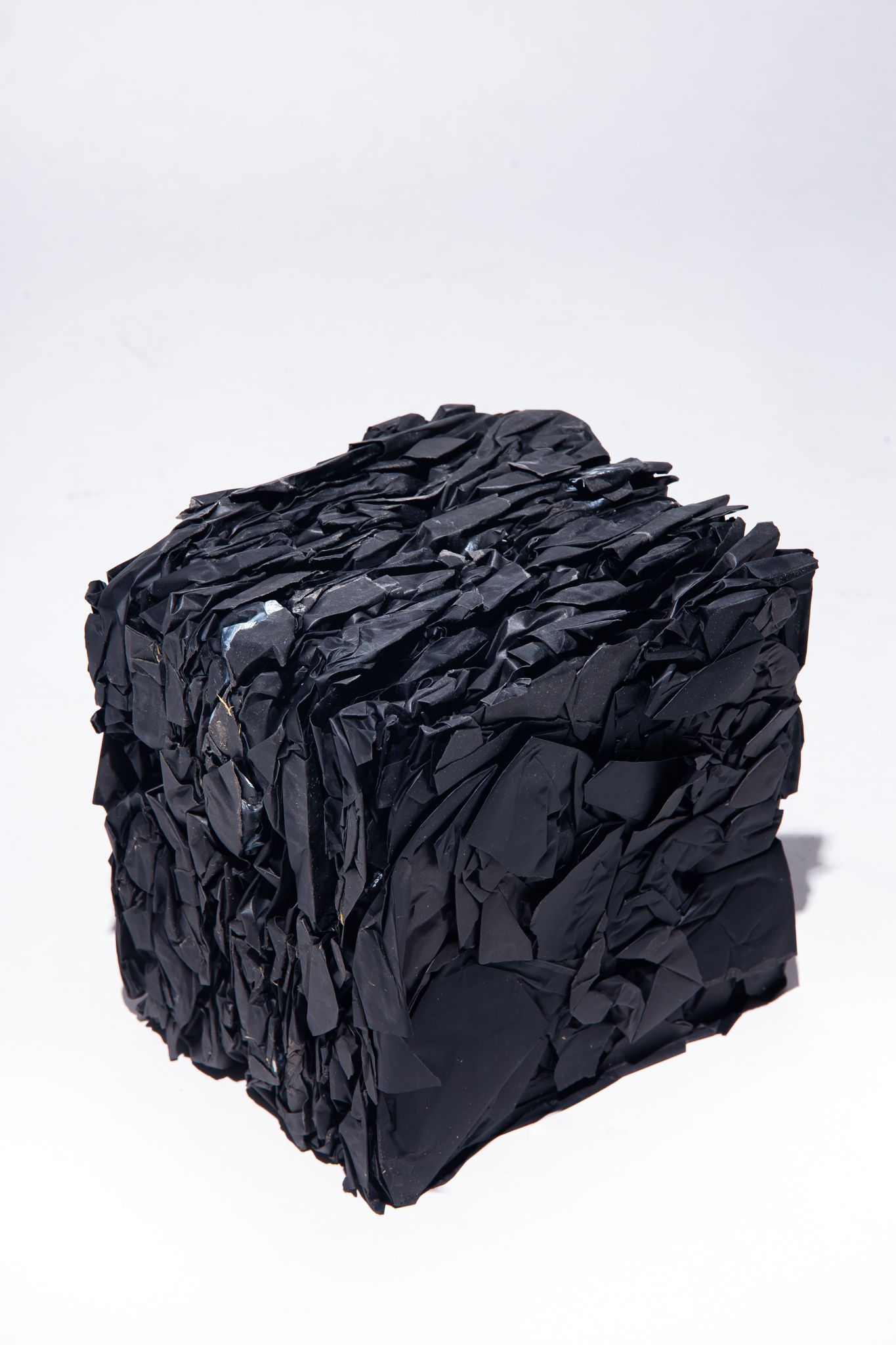 Black, cube-shaped artwork made of layered, irregularly-shaped dark pieces on a white background; art by Matt Remsbecher. 