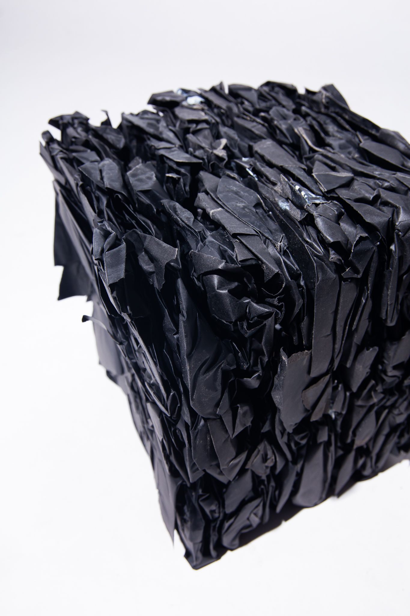 A compressed cube of black plastic bags against a white background; art by Matt Remsbecher. 
