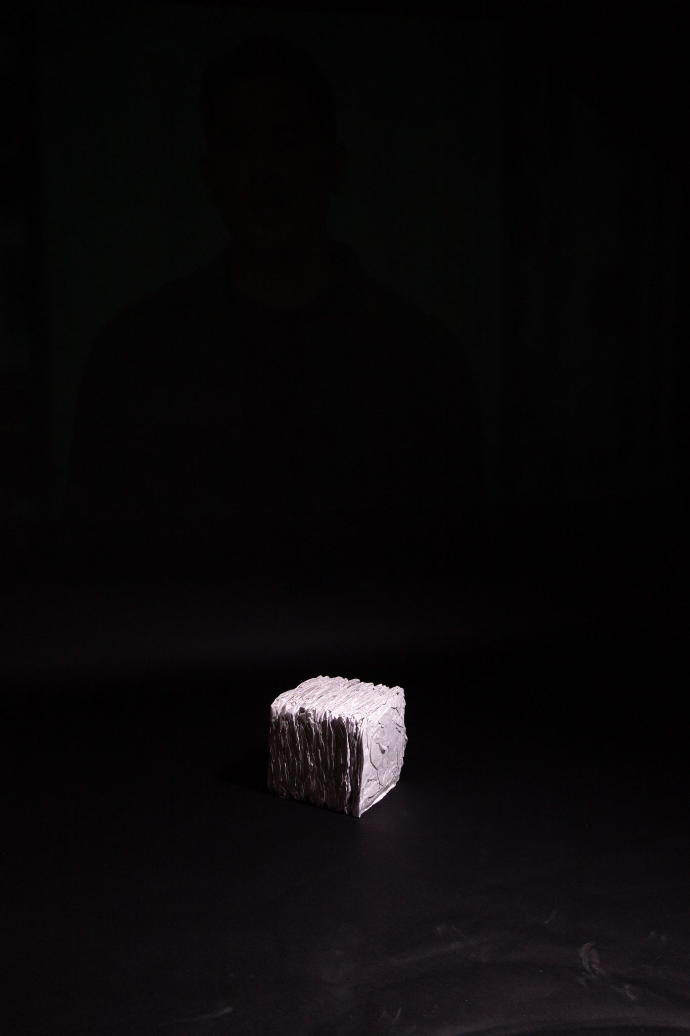 Cube-shaped object, possibly stone, against a dark black background; art by Matt Remsbecher. 