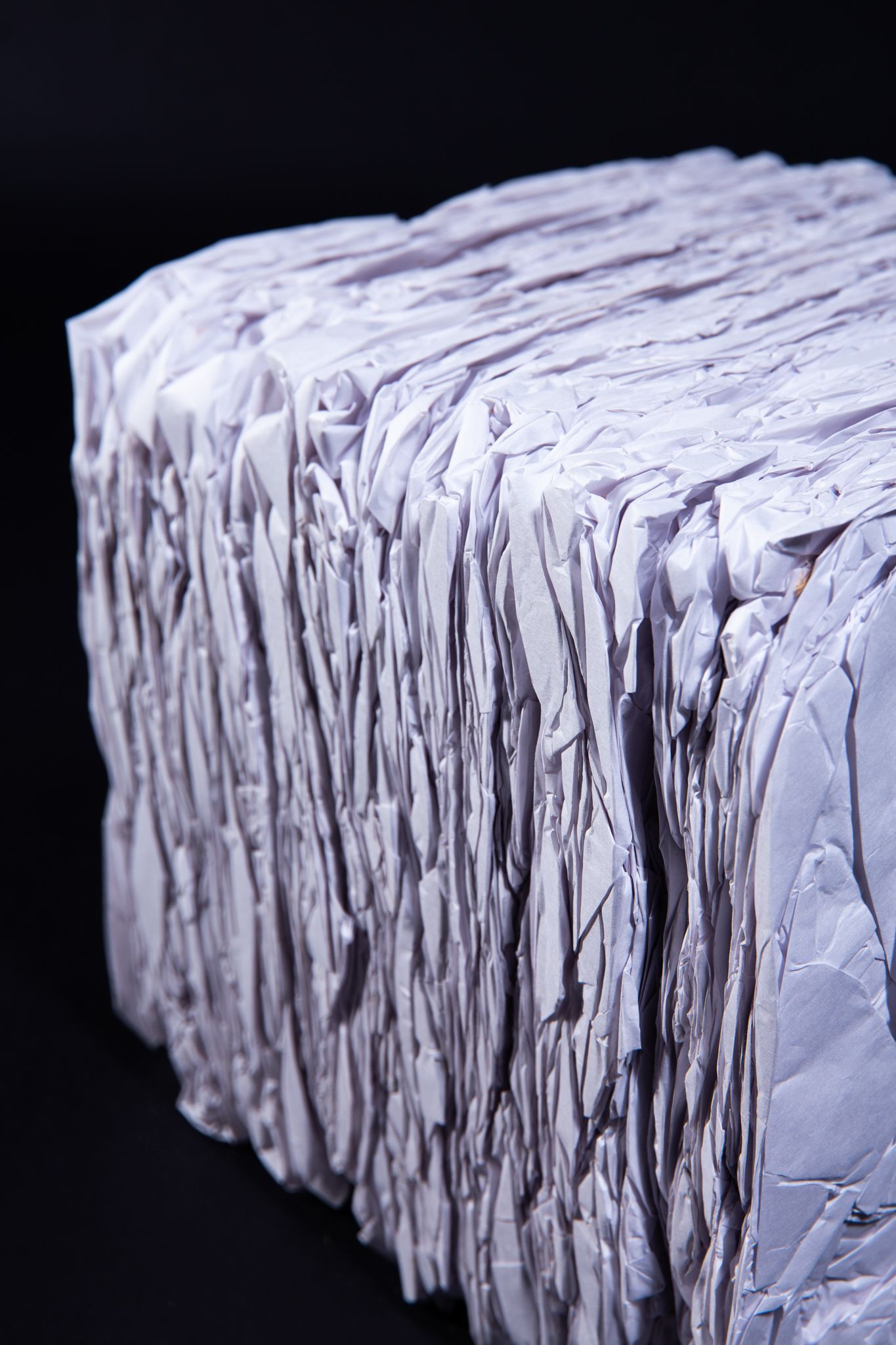 Cuboid bale of recycled paper, with jagged edges, in front of a dark background; art by Matt Remsbecher. 