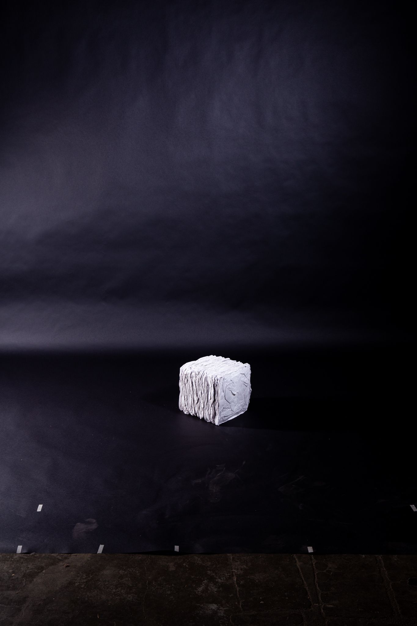 White, textured cube on black surface against a black backdrop, lit from above; art by Matt Remsbecher. 