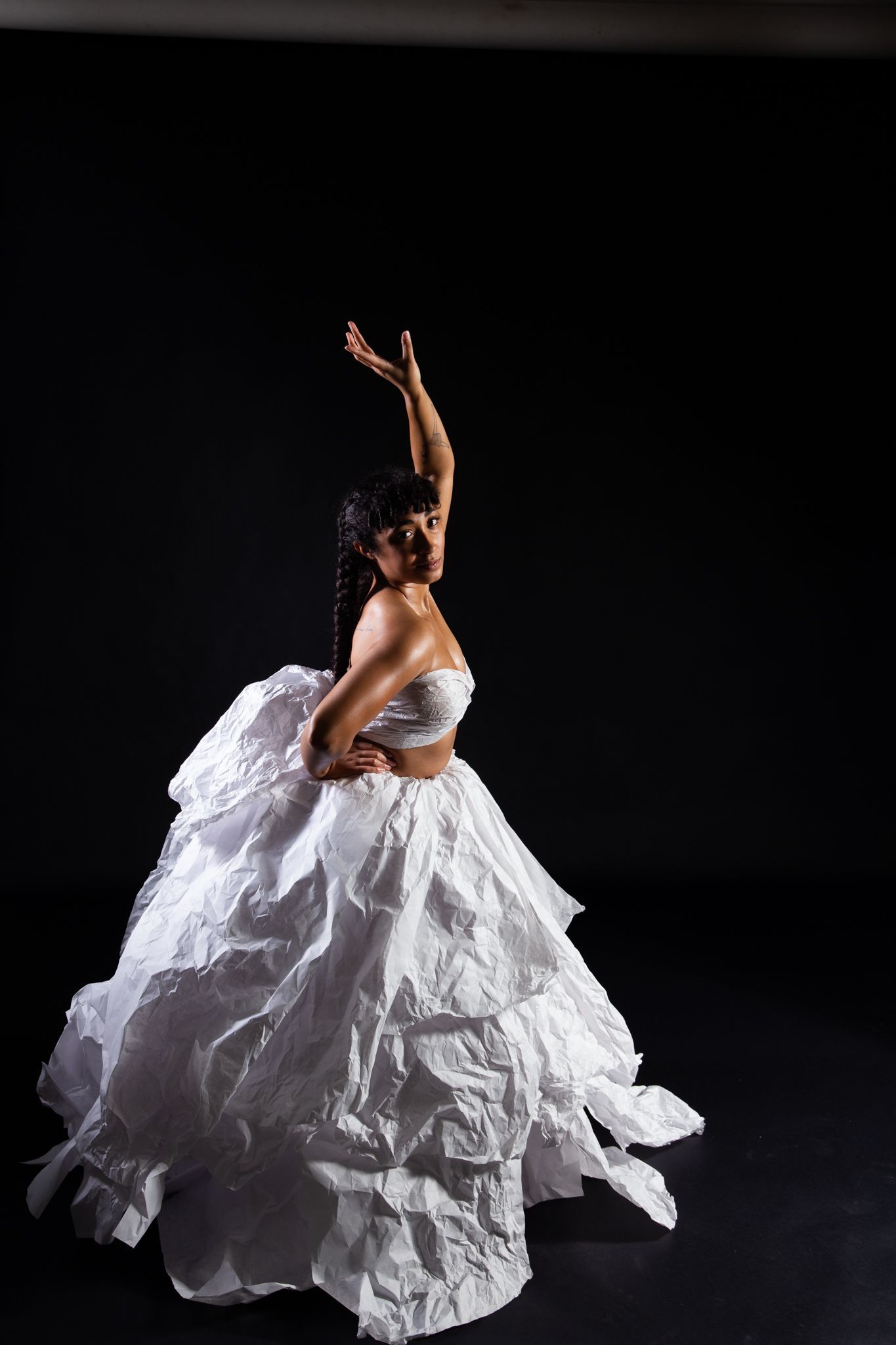 Woman in white dress, posed dance-like with arm raised, studio backdrop; art by Matt Remsbecher. 