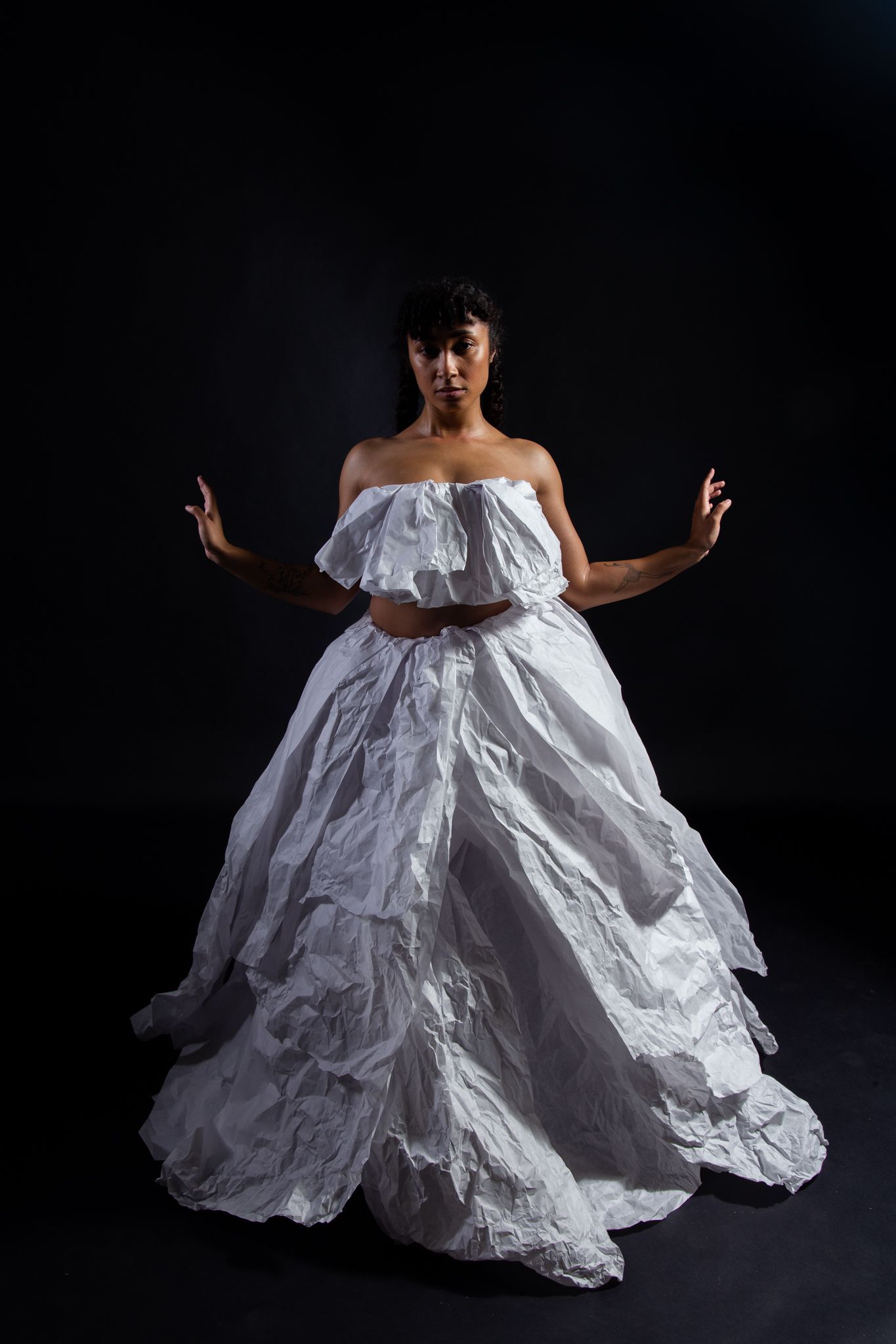 Woman in white, textured, layered gown with arms outstretched, set against a dark backdrop; art by Matt Remsbecher. 