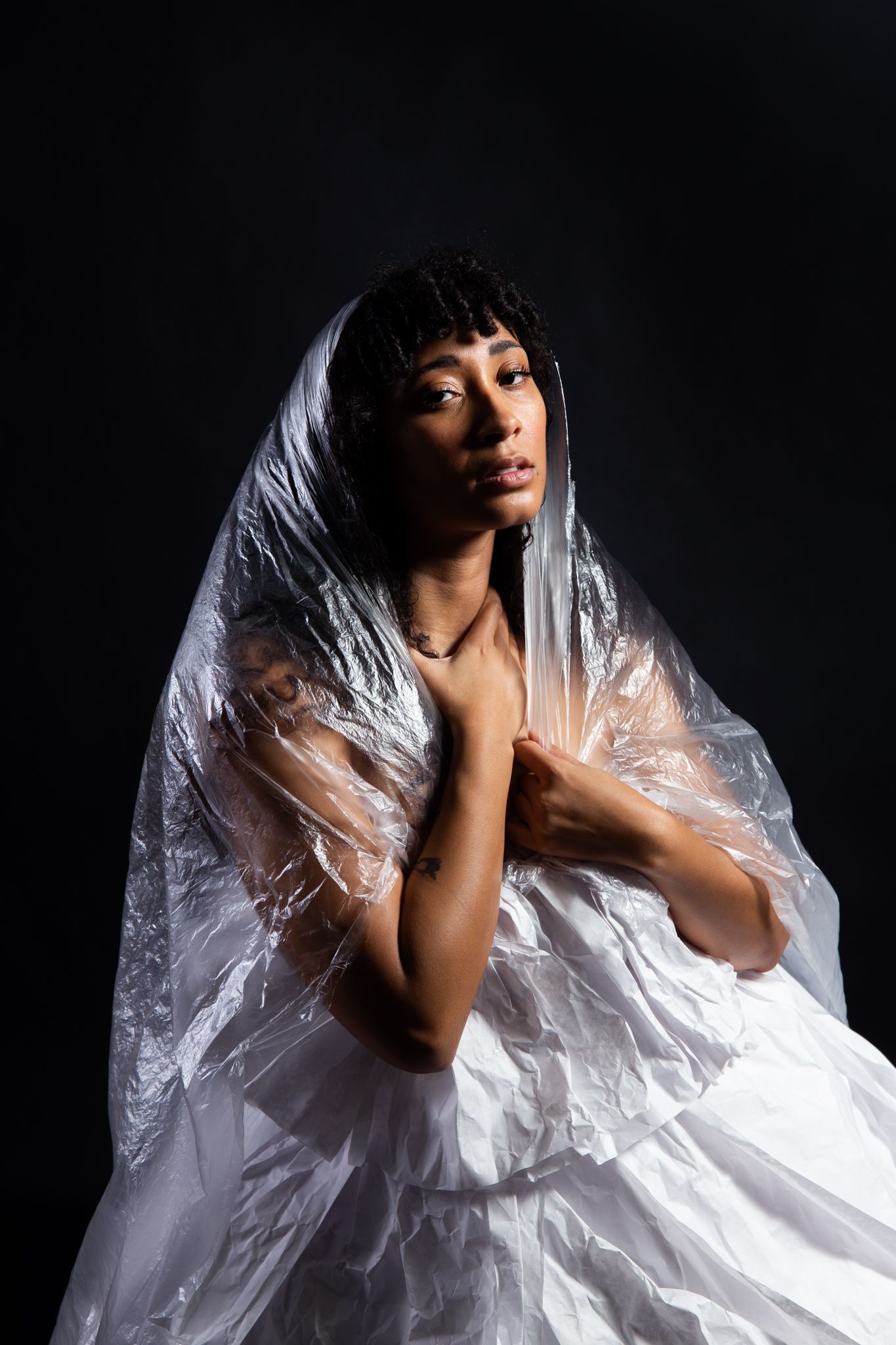 Woman in white dress and plastic wrap veil, hands on chest, dark background; art by Matt Remsbecher. 