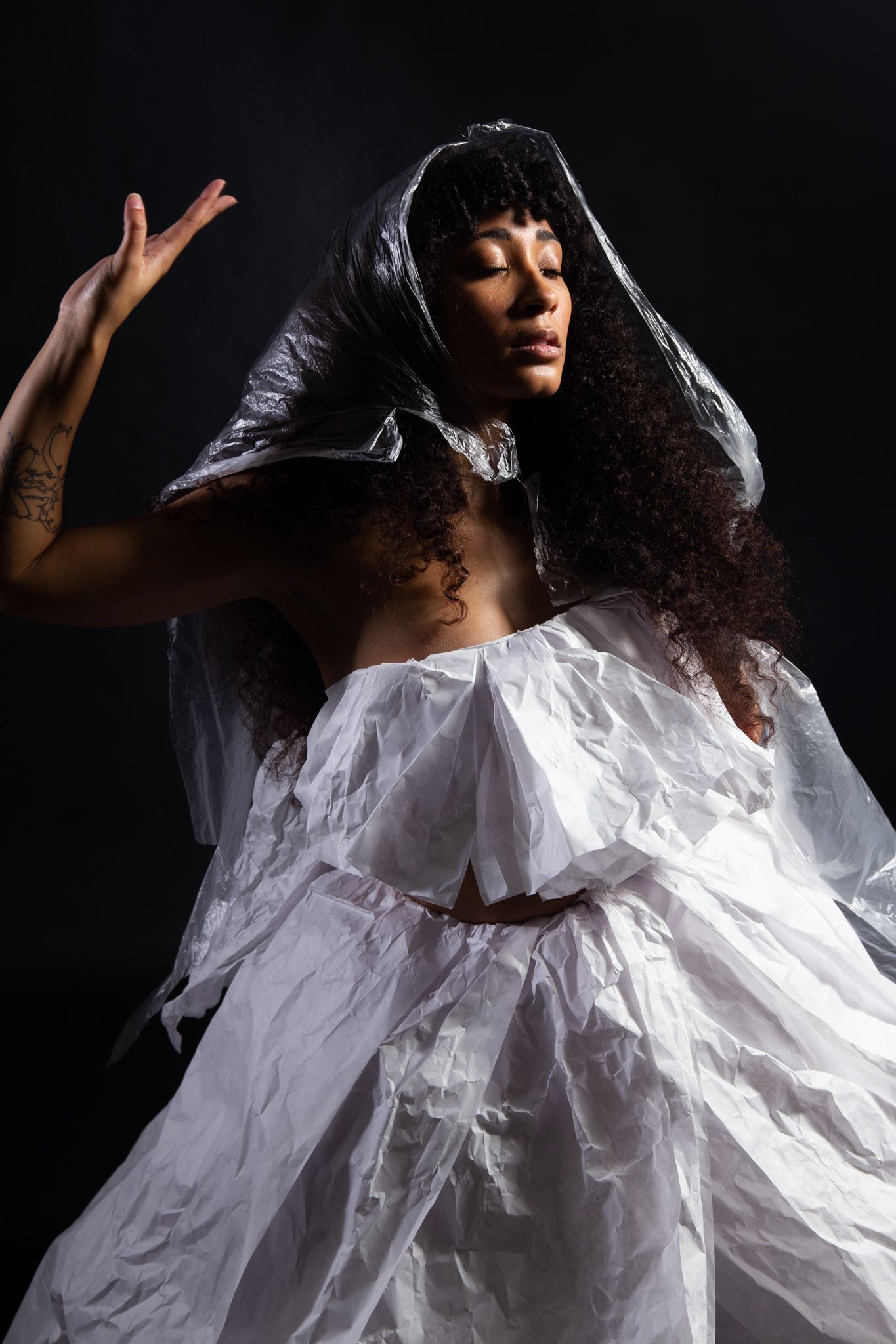 Woman in white, textured dress with head covering, arm raised, eyes closed, against dark background; art by Matt Remsbecher. 